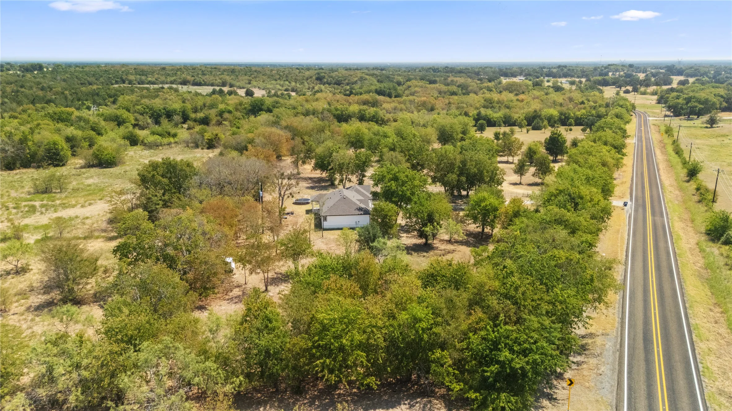 Rural property with a single-story dwelling, extensive tree coverage, and direct road frontage