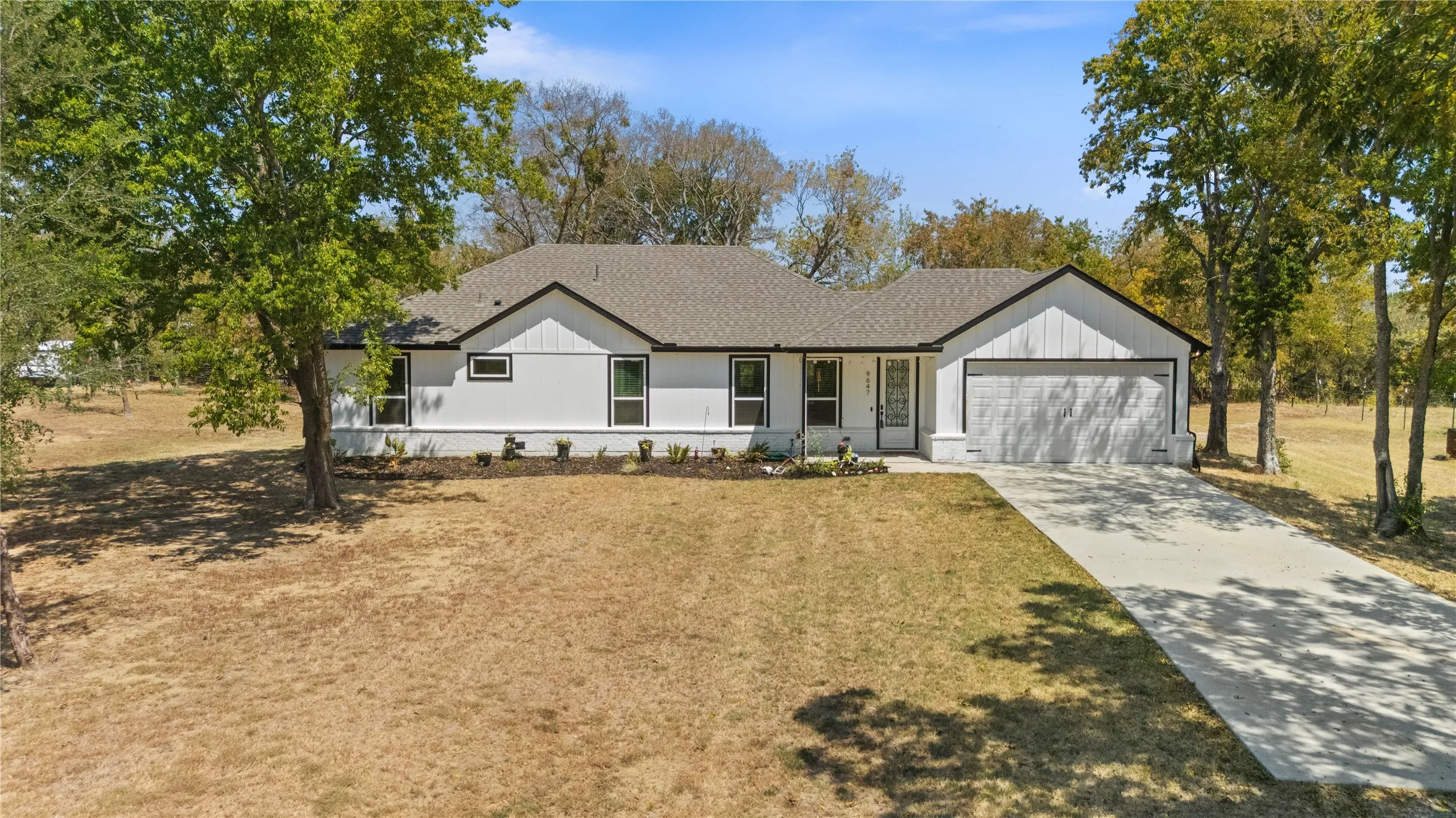 Charming ranch-style residence featuring a freshly paved driveway, attached two-car garage, and a sprawling front lawn shaded by mature trees