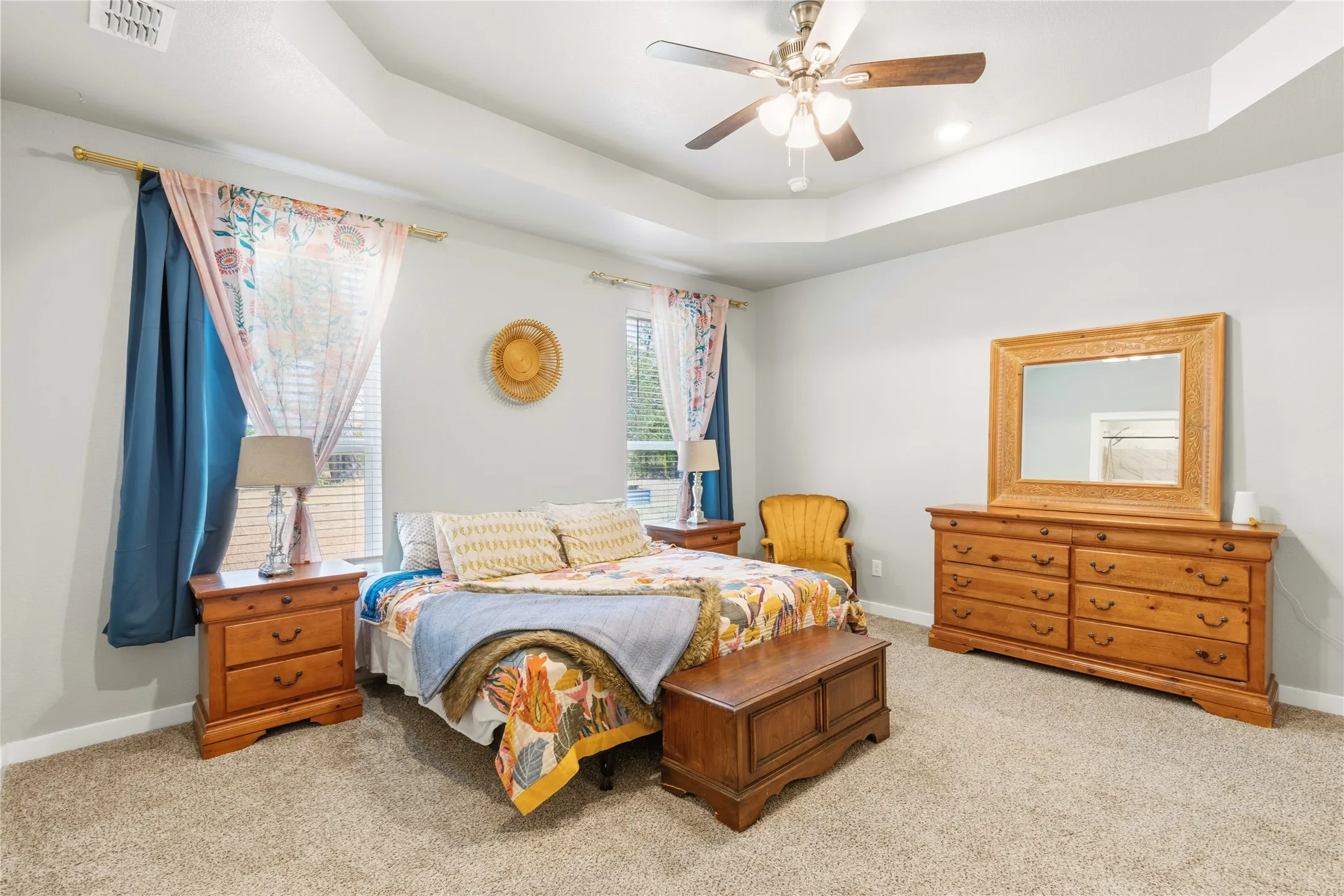 Tray ceiling with recessed lighting and a ceiling fan, light-toned carpeting, and windows with blinds