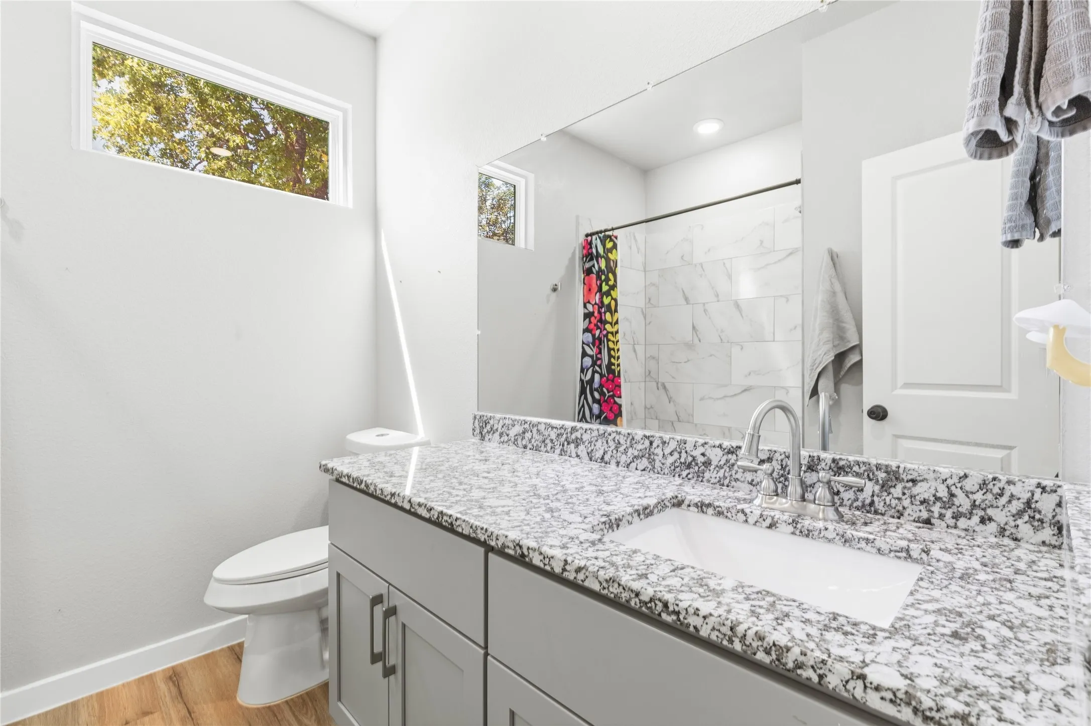 Contemporary bathroom featuring a vanity with a white rectangular undermount sink, speckled countertop, and wood-finish flooring