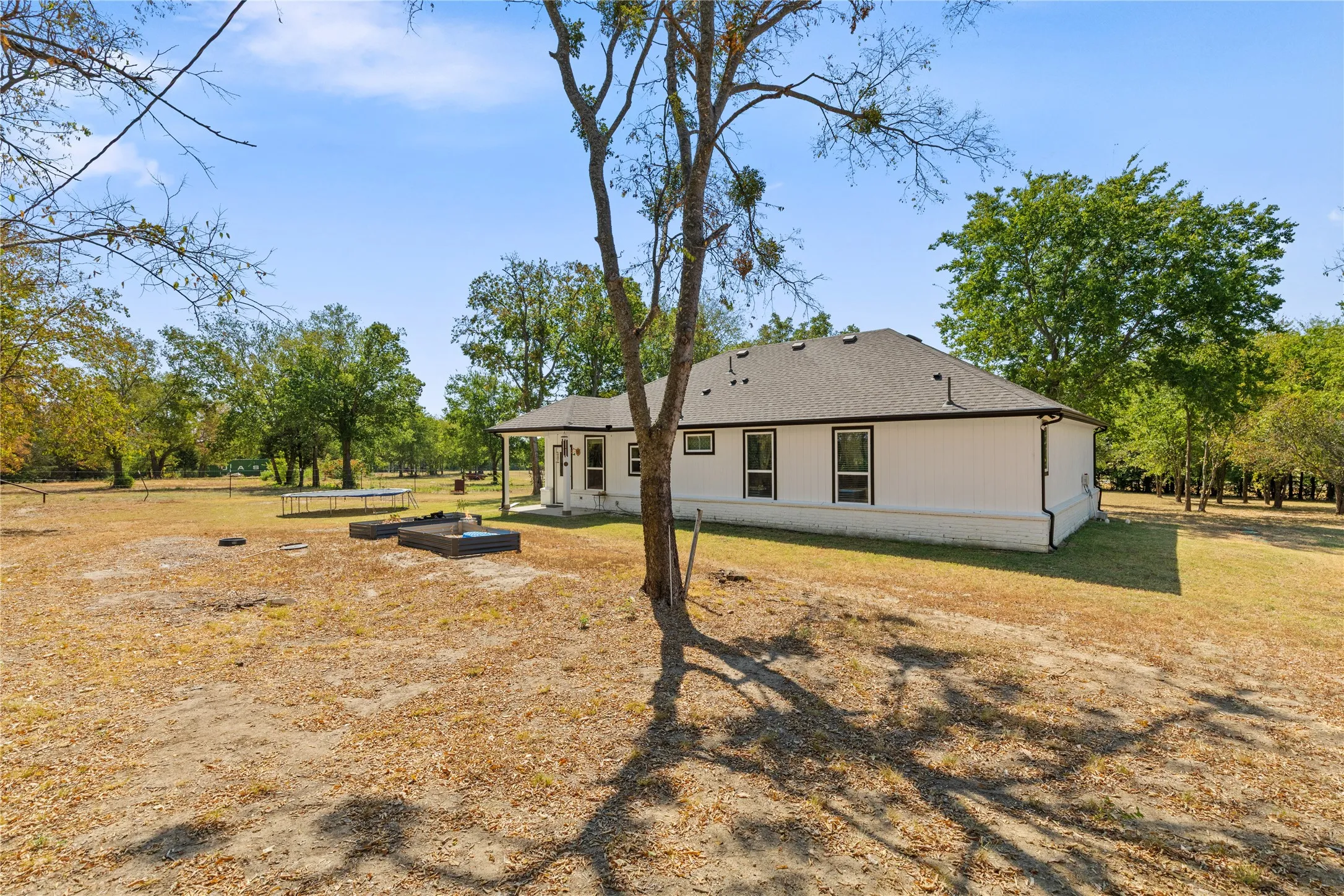 White exterior with black trim windows, covered porch, and expansive yard