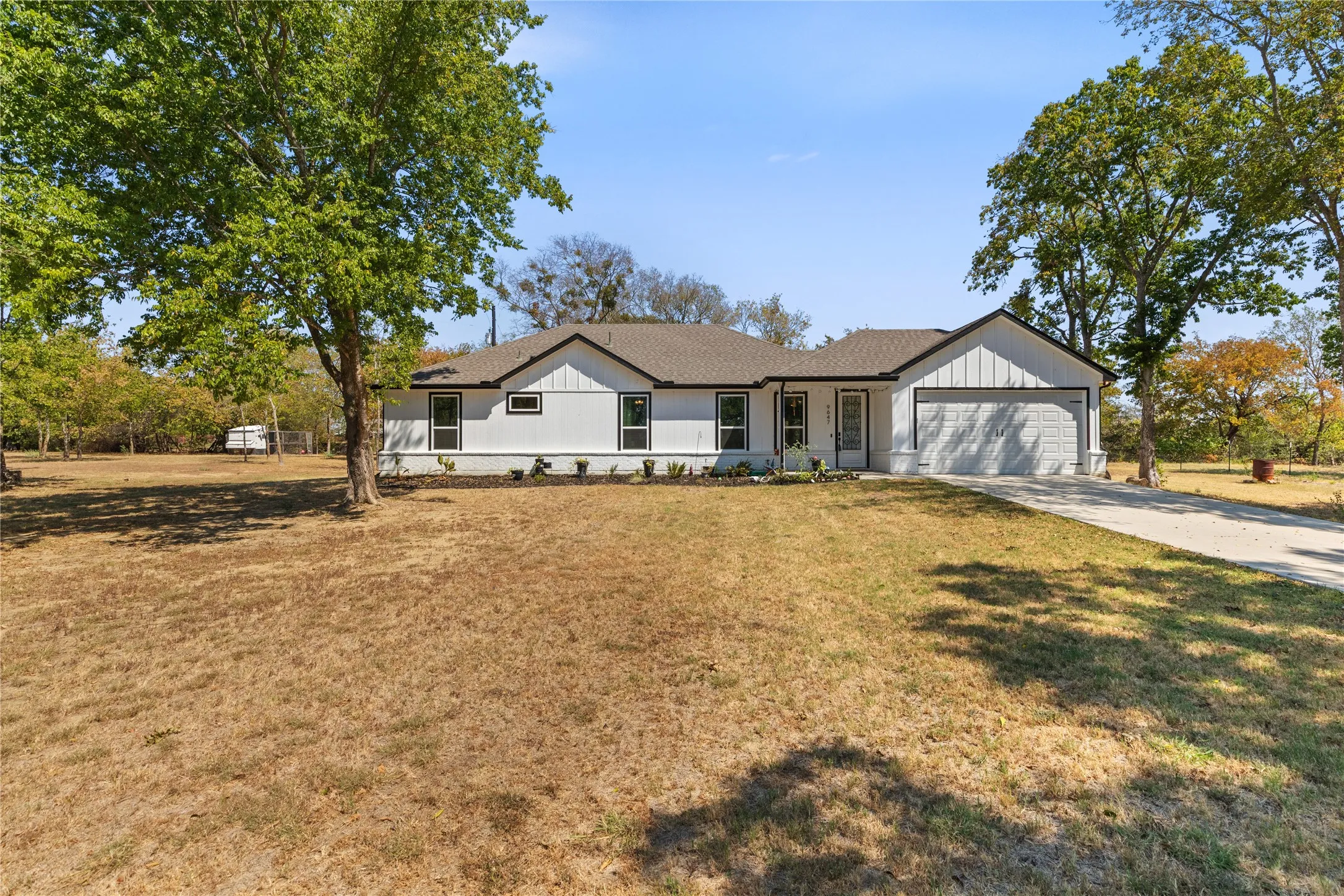 White board-and-batten exterior with contrasting trim, two-car garage, mature trees, and a concrete driveway