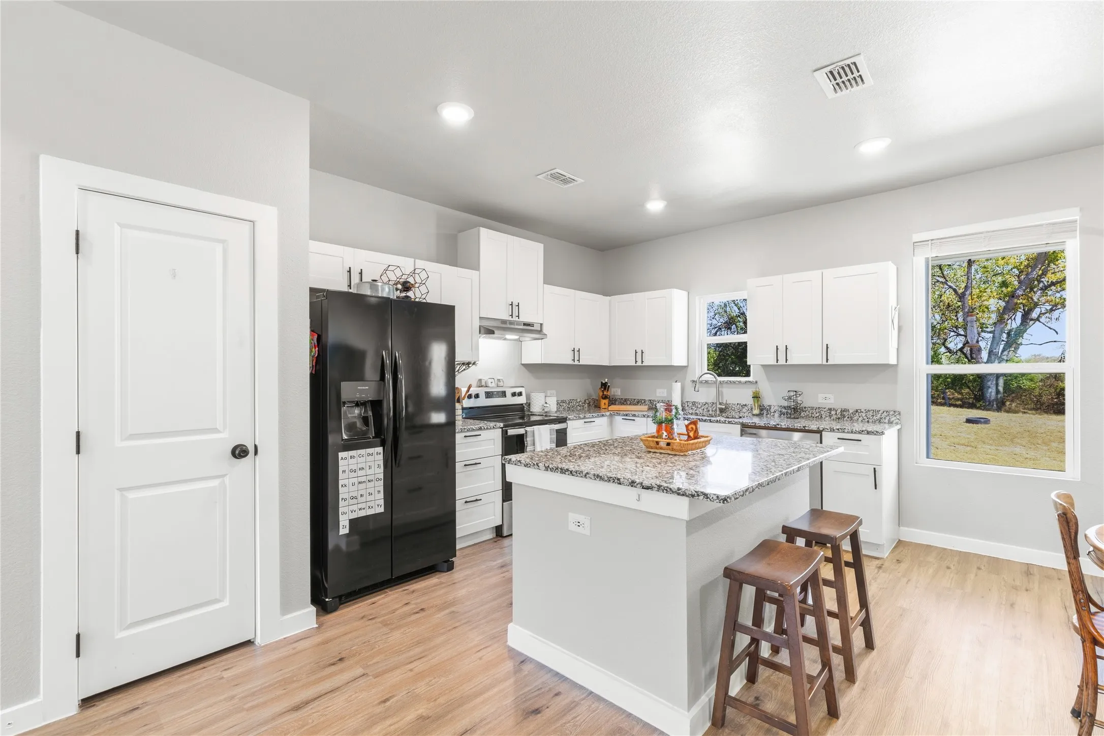 Kitchen featuring wood-finish flooring, white cabinetry, a center island with bar seating, and granite countertops
