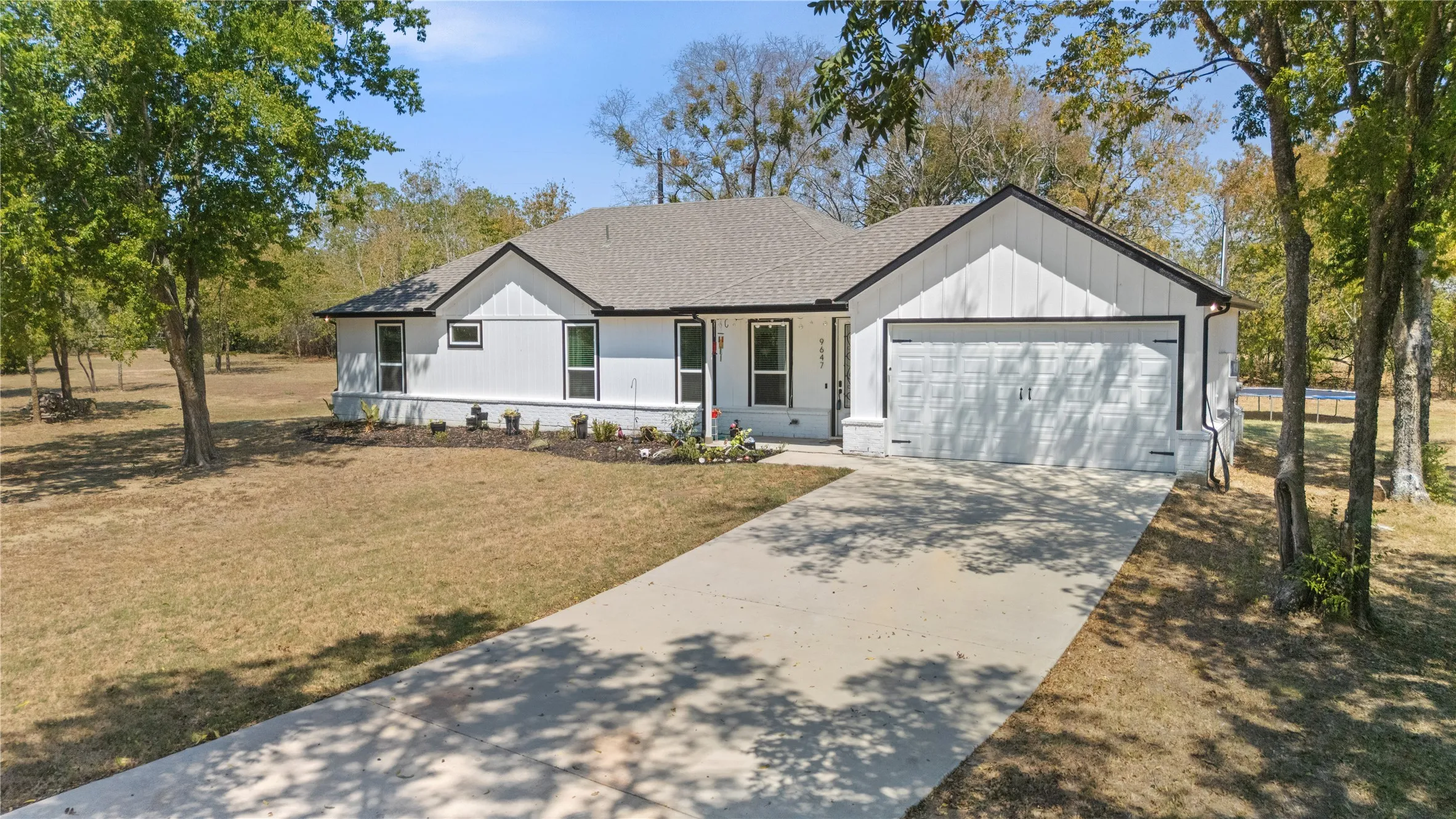 Modern farmhouse exterior with white vertical siding, black trim, a gabled roofline, and an attached two-car garage