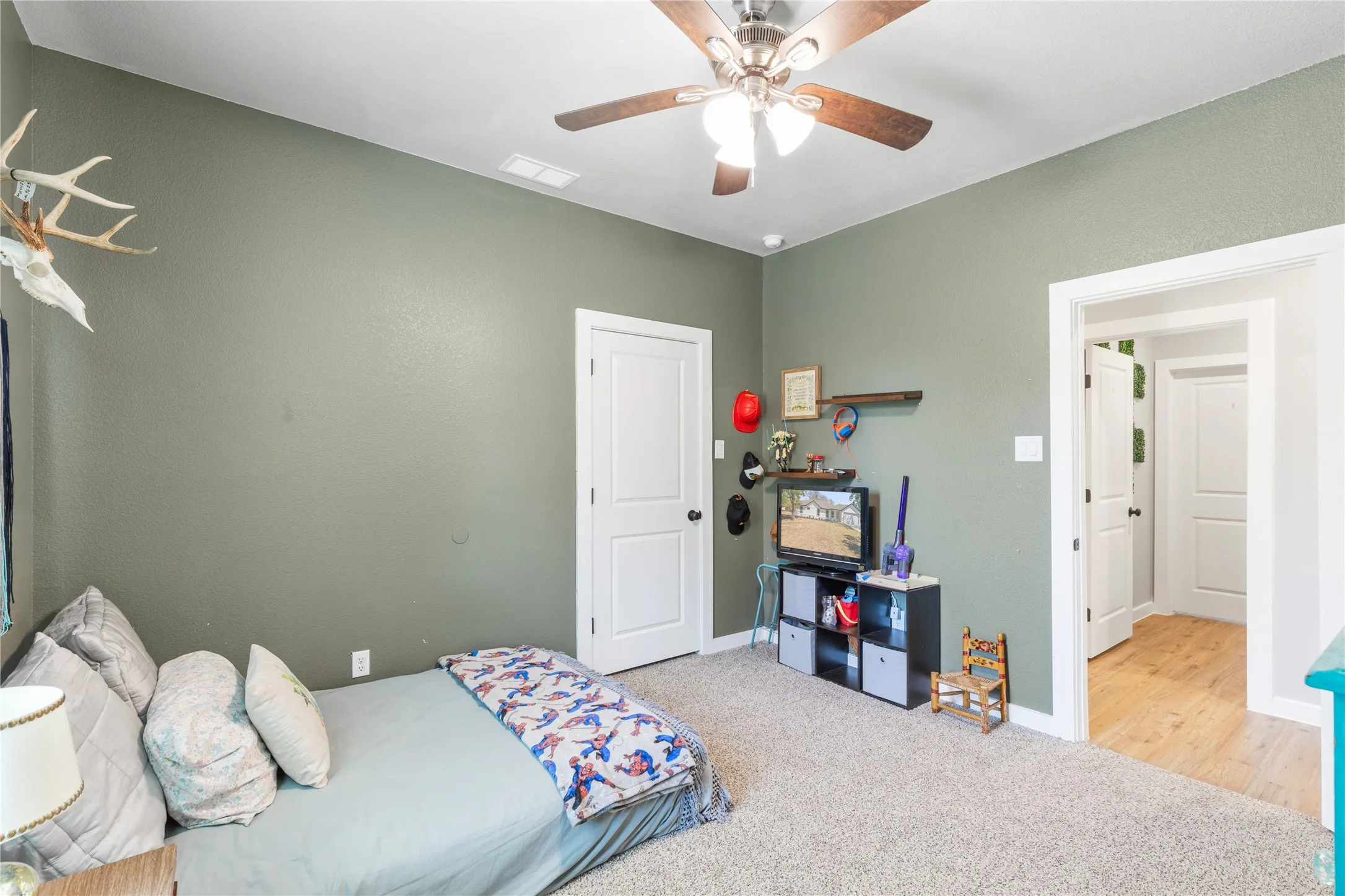 Carpeted room featuring a ceiling fan with light fixture and a solid white door