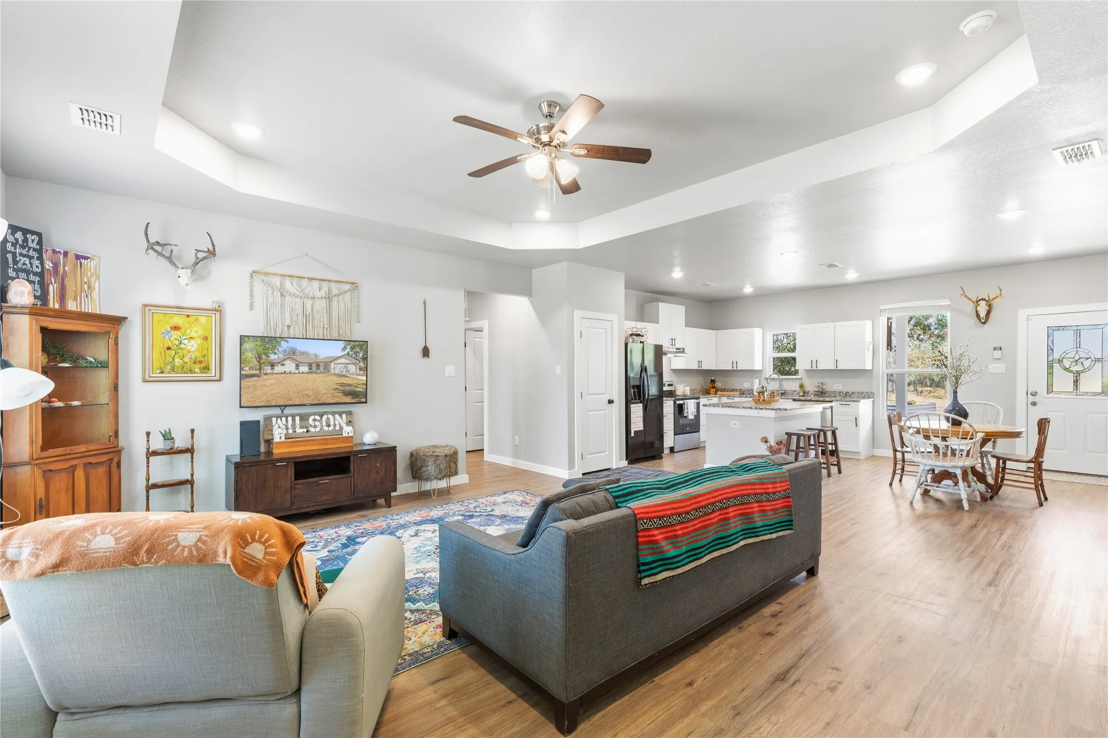 Tray ceiling with recessed lighting, wood-finish flooring, white kitchen cabinetry, kitchen island with breakfast bar, and a decorative glass-paneled entry door