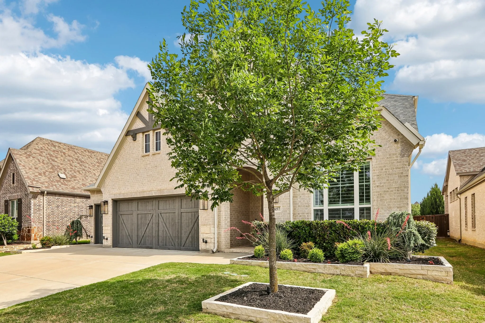 Brick exterior with stone accents, gable roofline, decorative garage door, and established landscaping