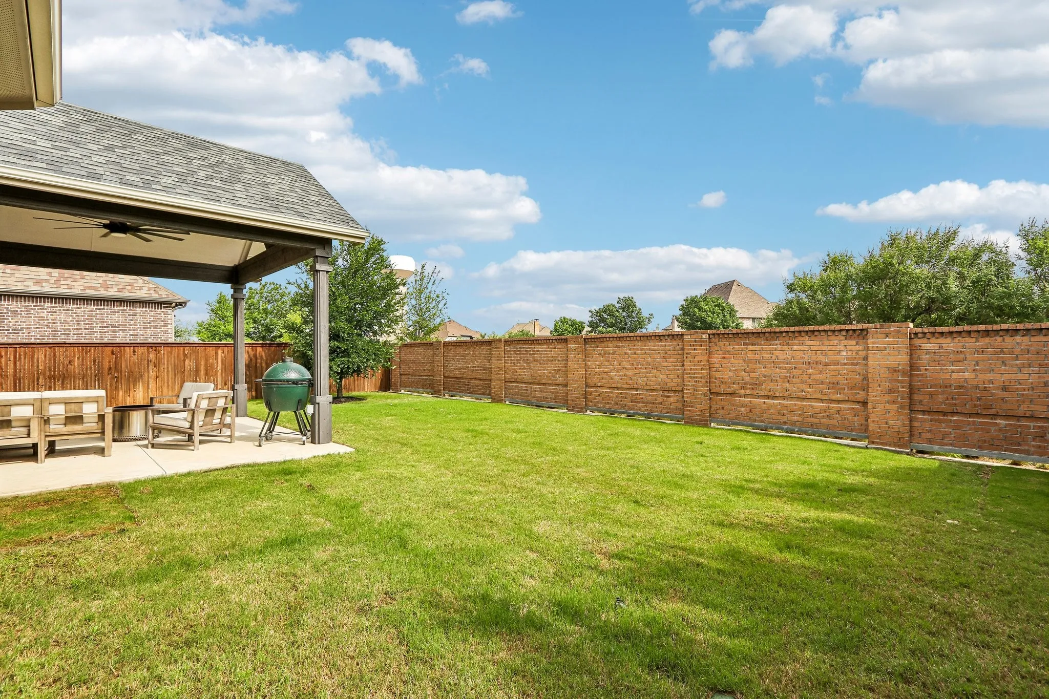 Expansive lawn with a covered patio, featuring an outdoor ceiling fan, and a wood privacy fence