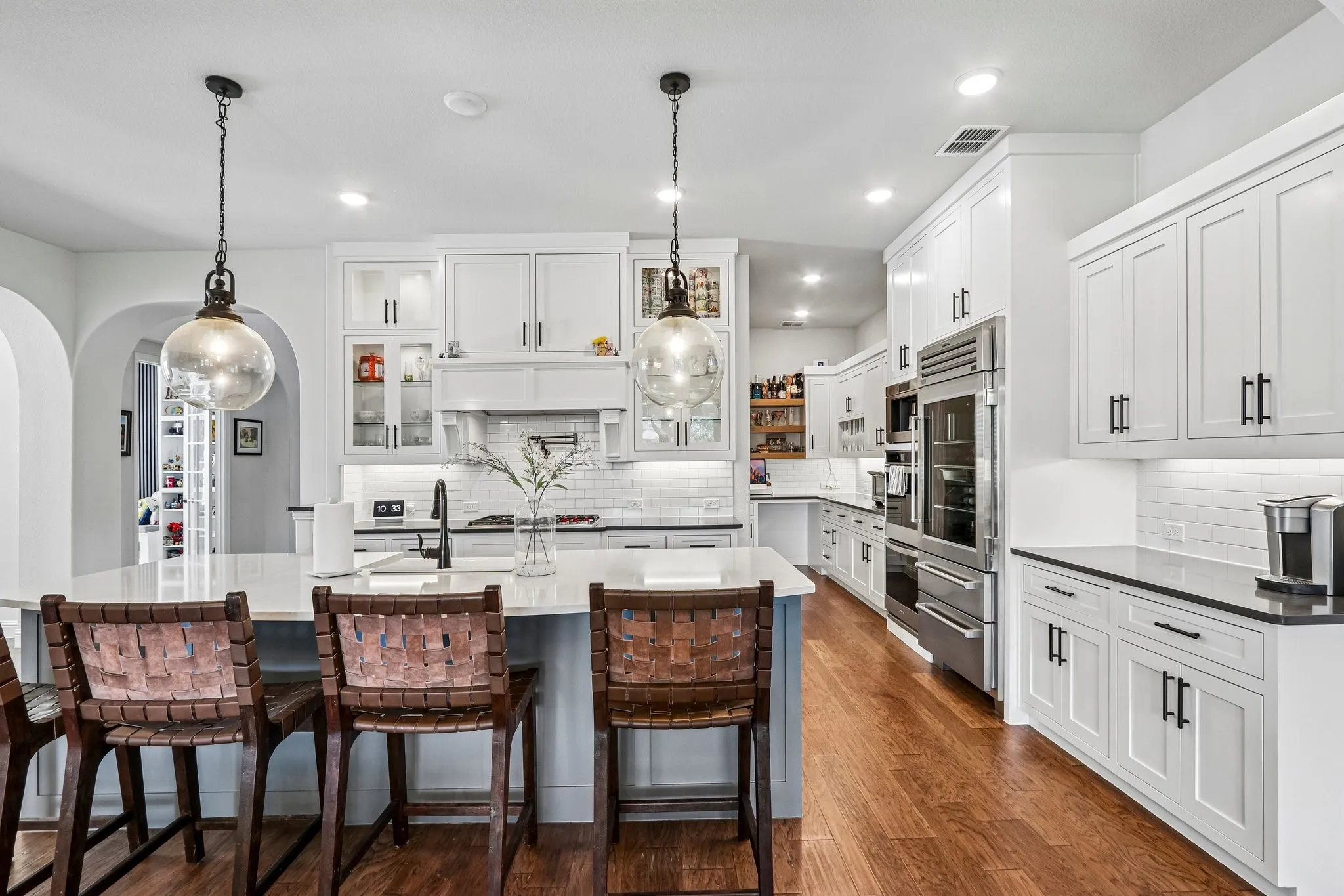 Spacious kitchen featuring white cabinetry, stainless steel appliances, a large center island, wood-finish flooring, and subway tile backsplash