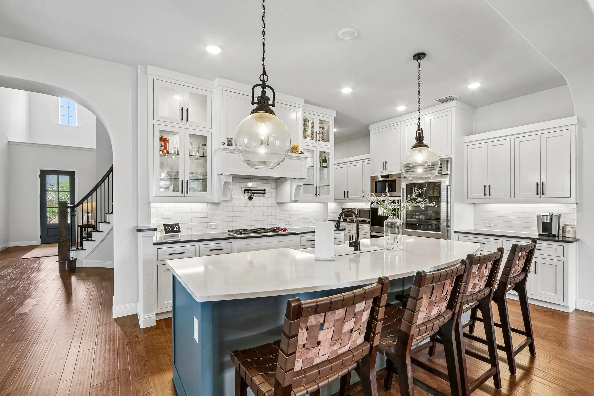 Gourmet kitchen with white cabinetry, a large center island with seating, built-in stainless steel appliances, and wood-finish flooring