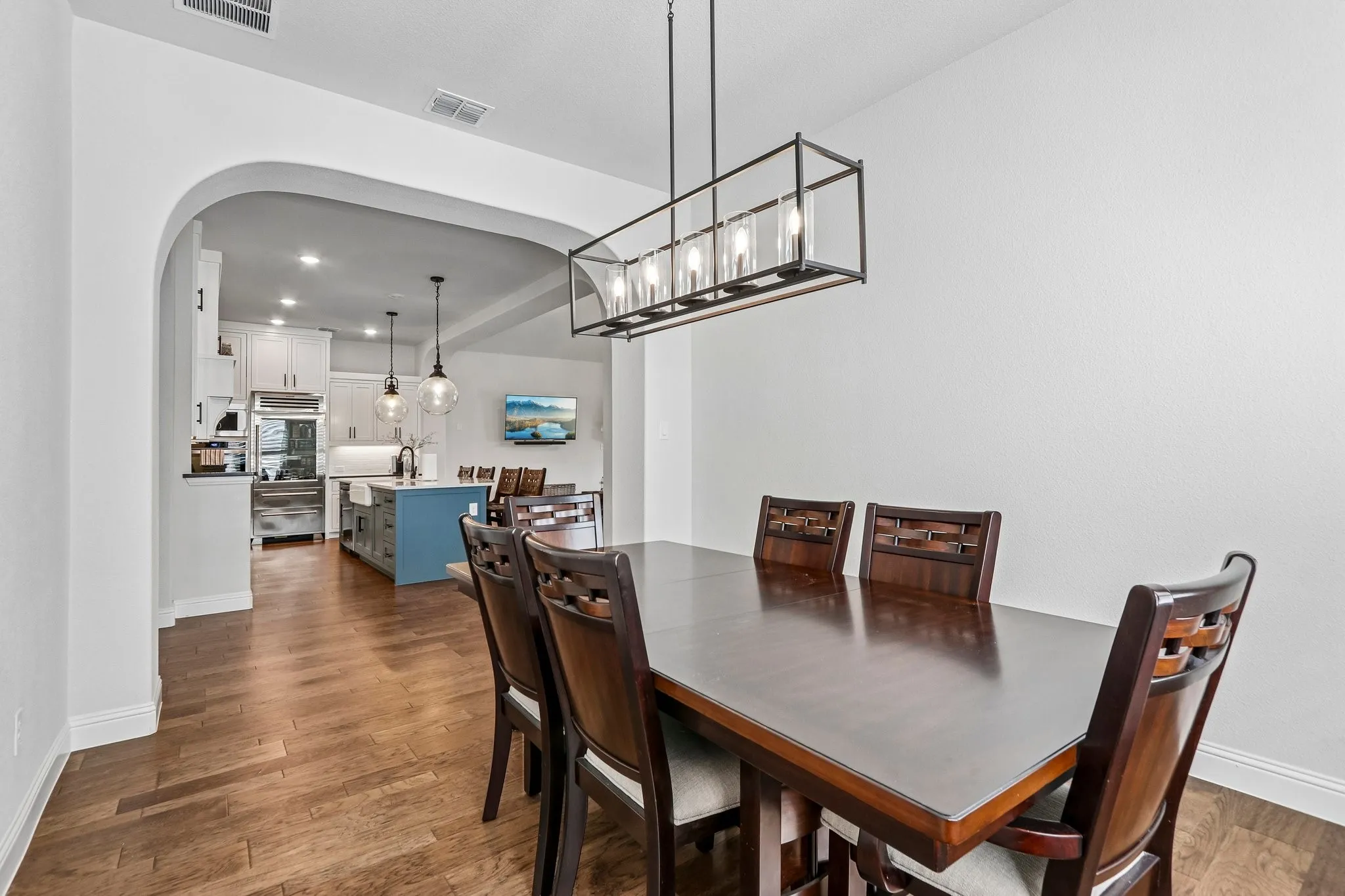 Arched entryway leading to a kitchen with stainless steel appliances, a center island with a built-in sink, and pendant lighting