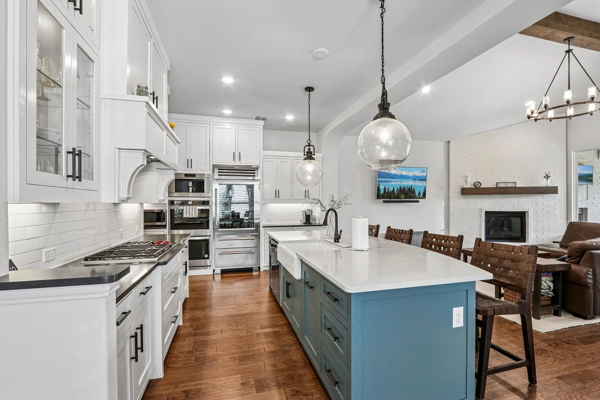 Gourmet kitchen featuring a white subway tile backsplash, stainless steel appliances, a large center island with a farm sink, and wood-finish flooring