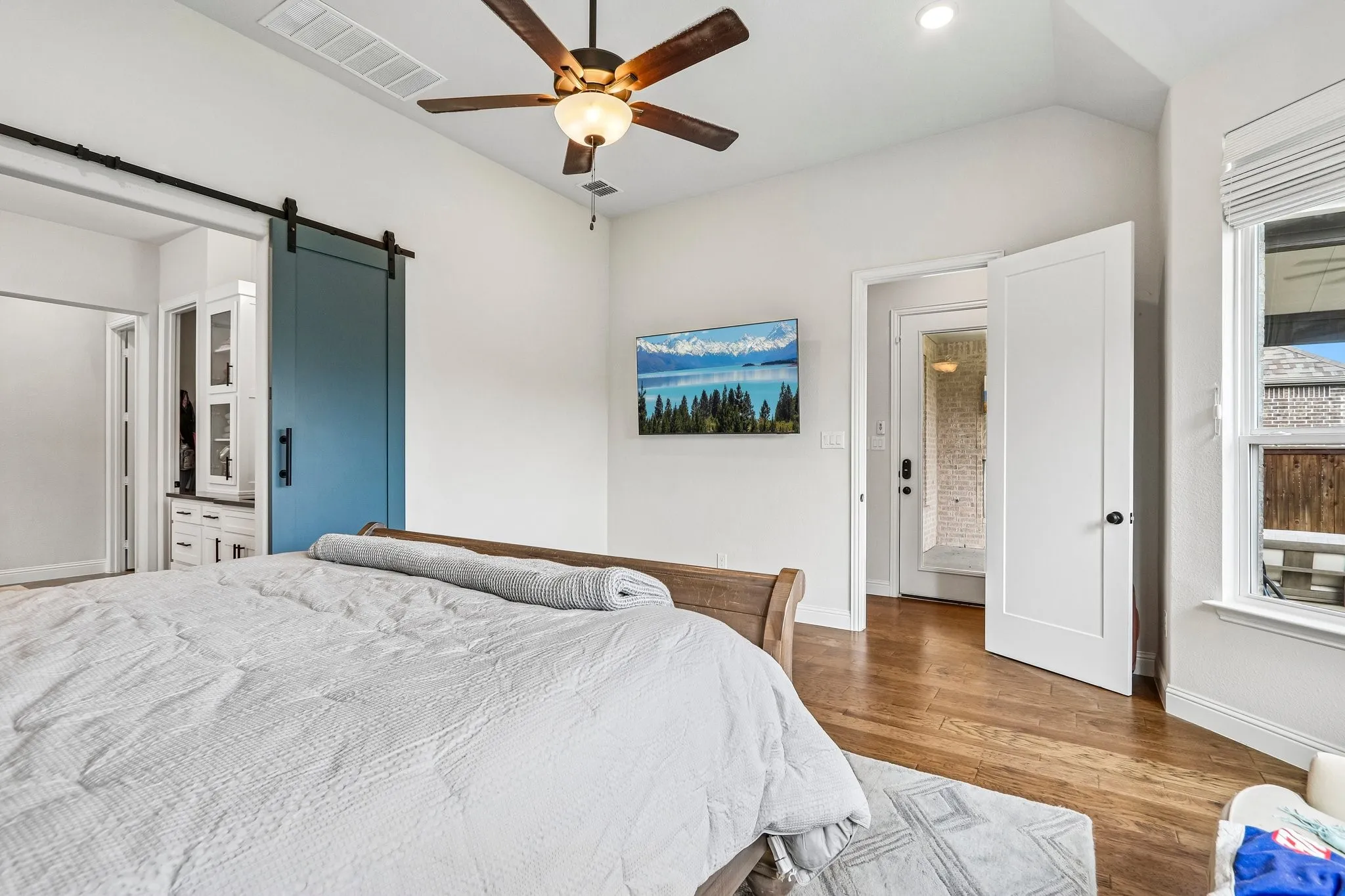 Vaulted ceiling with a ceiling fan, hardwood flooring, white paneled door, and a blue barn door
