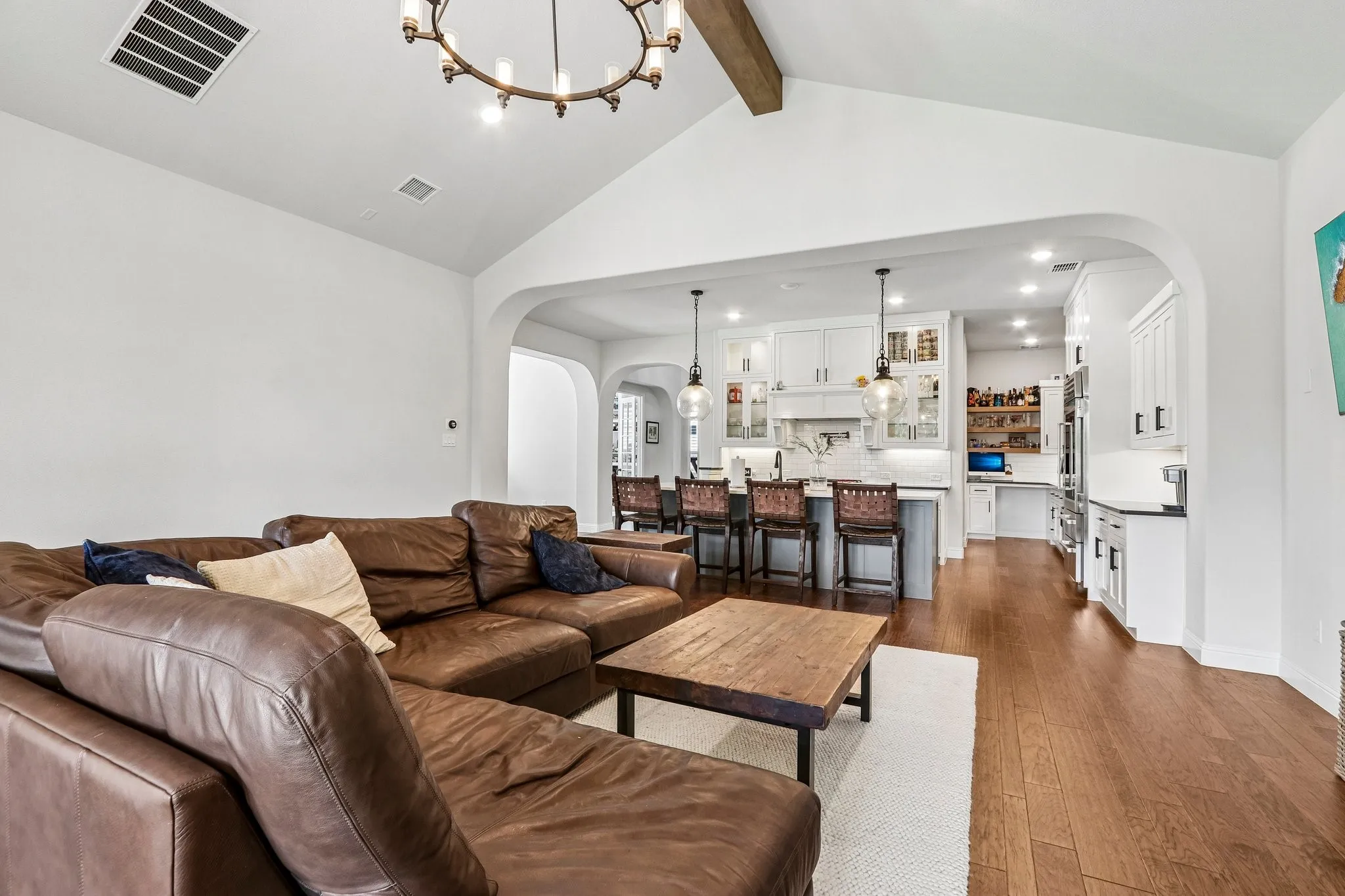 Vaulted ceiling with an exposed beam, hardwood flooring, recessed lighting, arched doorways, and a kitchen featuring white cabinetry