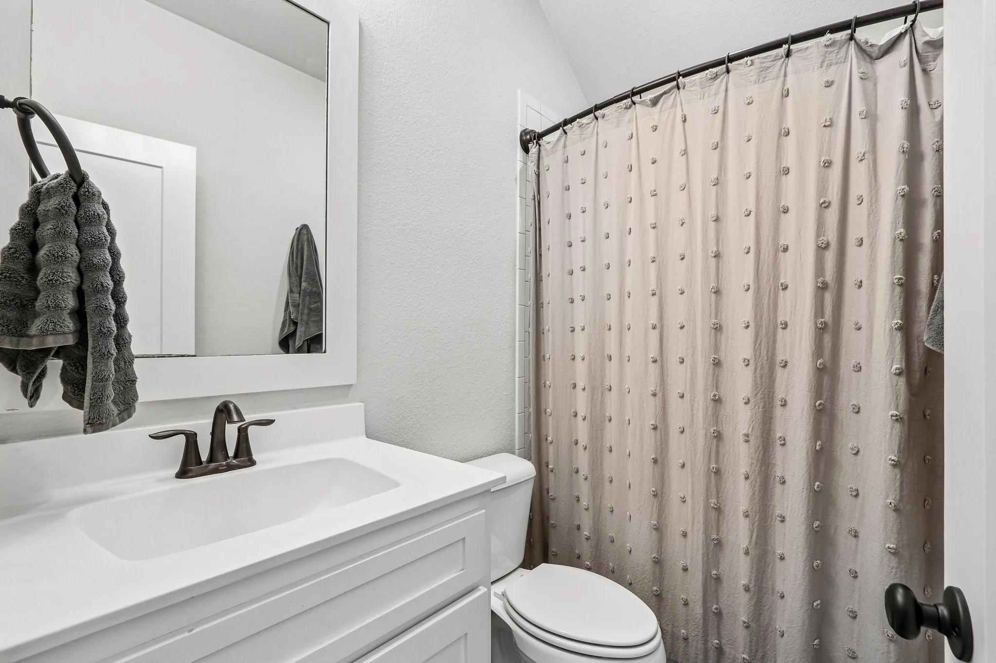 White vanity with integrated sink, bronze-finish faucet, and coordinating mirror