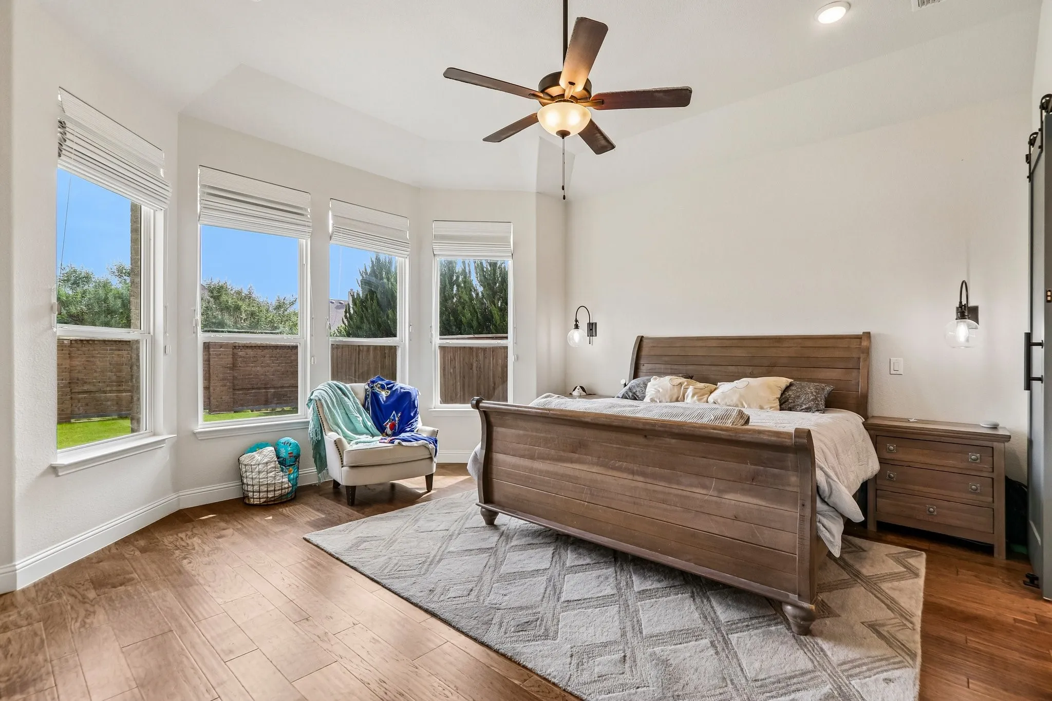 Bay window with multiple large windows, wood-finish flooring, recessed lighting, ceiling fan, and wall-mounted sconces