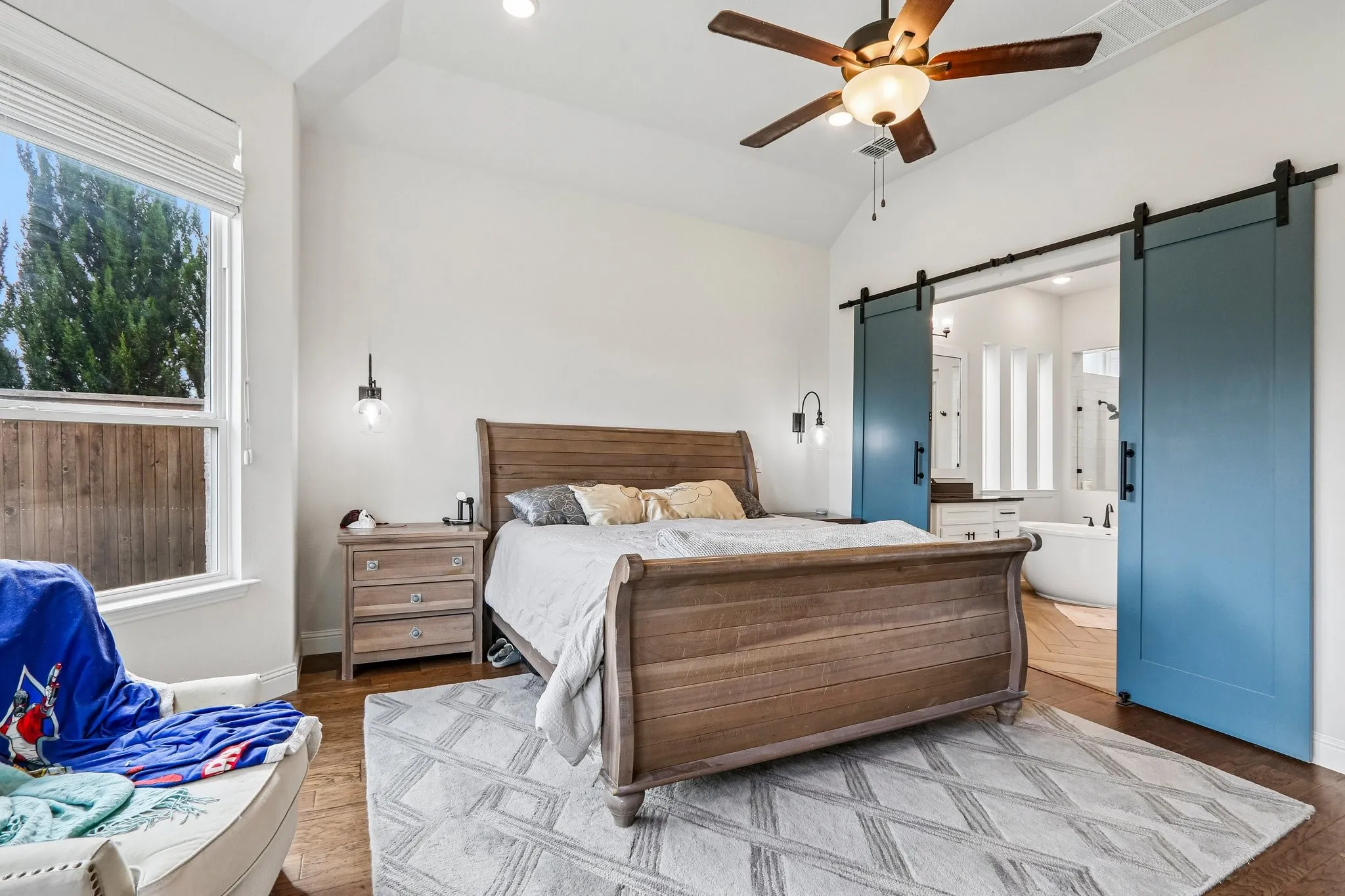 Vaulted ceiling with a ceiling fan, wood-finish flooring, recessed lighting, and wall-mounted sconces
