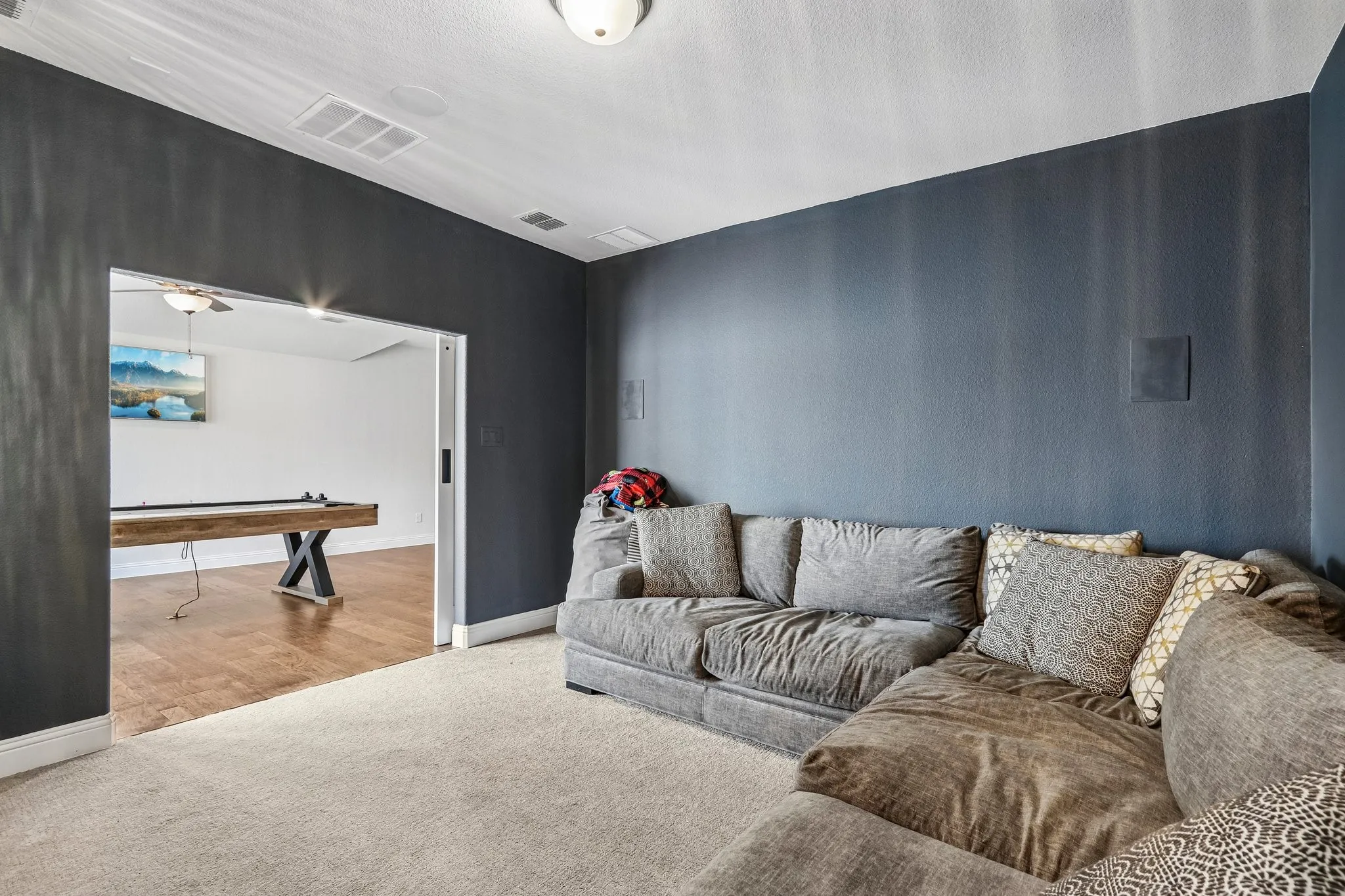 Recessed speaker system, overhead flush mount light fixture, carpeting, wood-finish flooring in adjacent room, and wide entryway