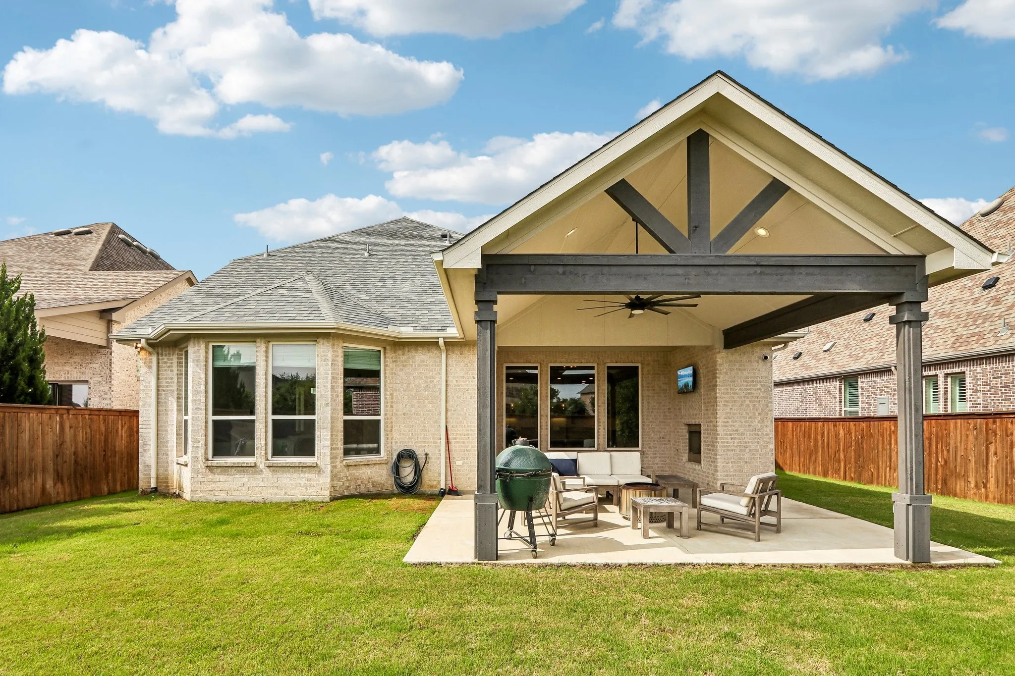 Expansive backyard featuring a covered patio, vaulted ceiling with exposed beams, ceiling fan, and brick​​‌​​​​‌​​‌‌​‌‌​​​‌‌​‌​‌​‌​​​‌​​ fireplace