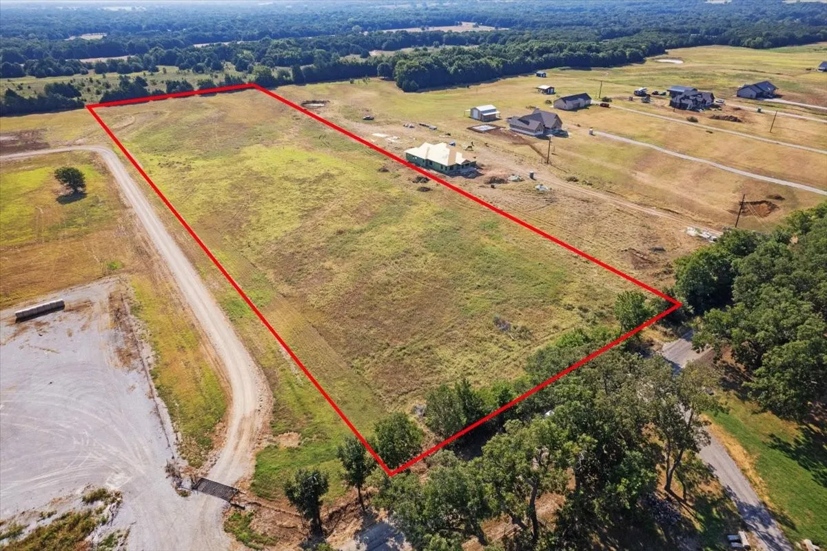 Expansive lot featuring a cleared building site, mature perimeter trees, and a gravel driveway