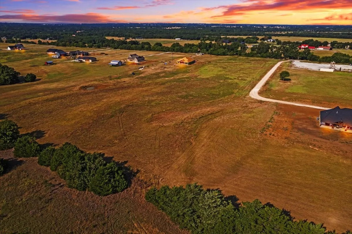 Expansive rural landscape featuring a private gravel driveway, scattered mature trees, and multiple residences