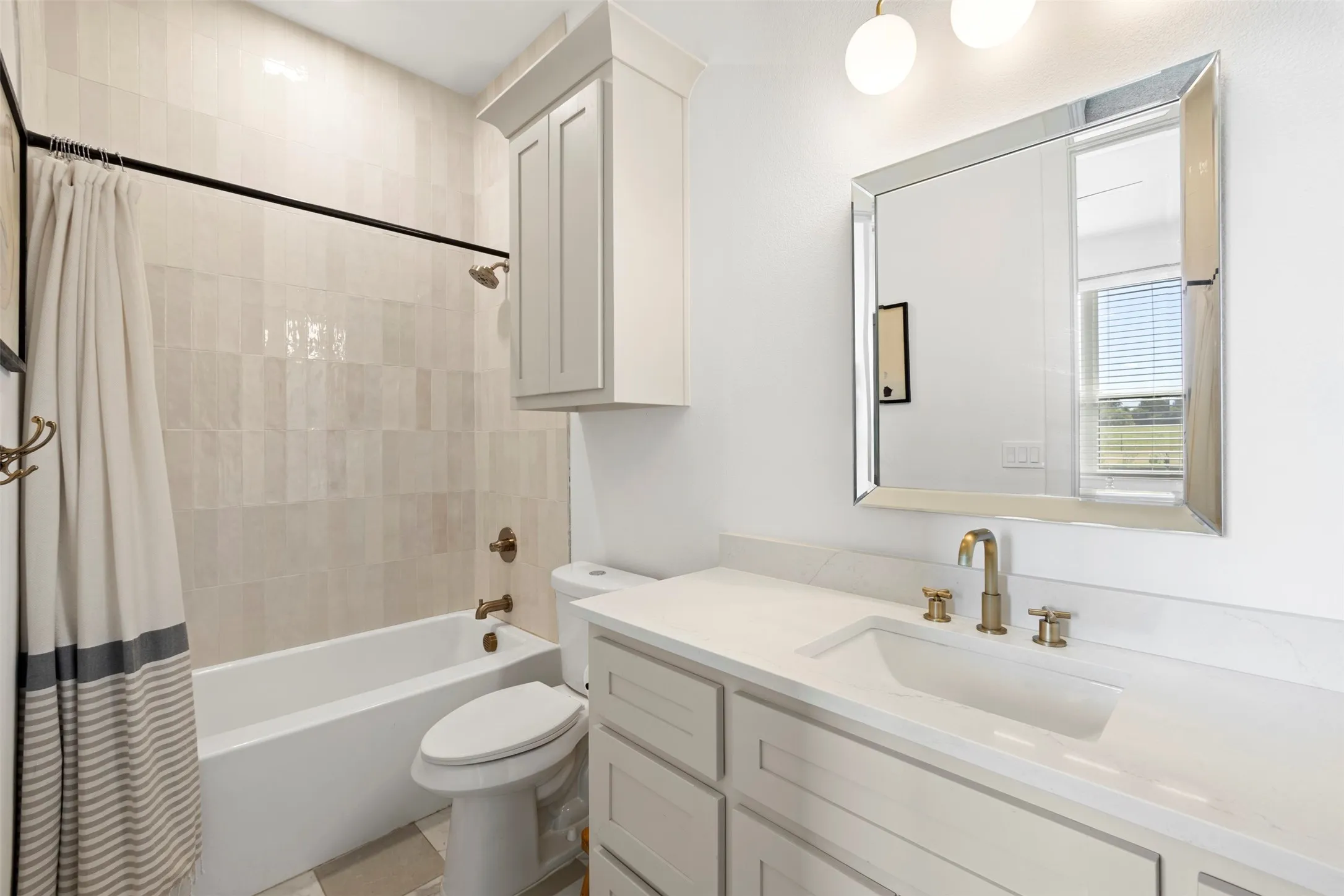 Full bathroom featuring a single vanity with stone countertop, undermount sink, brass-finish fixtures, and a tub-shower combination with floor-to-ceiling tile surround