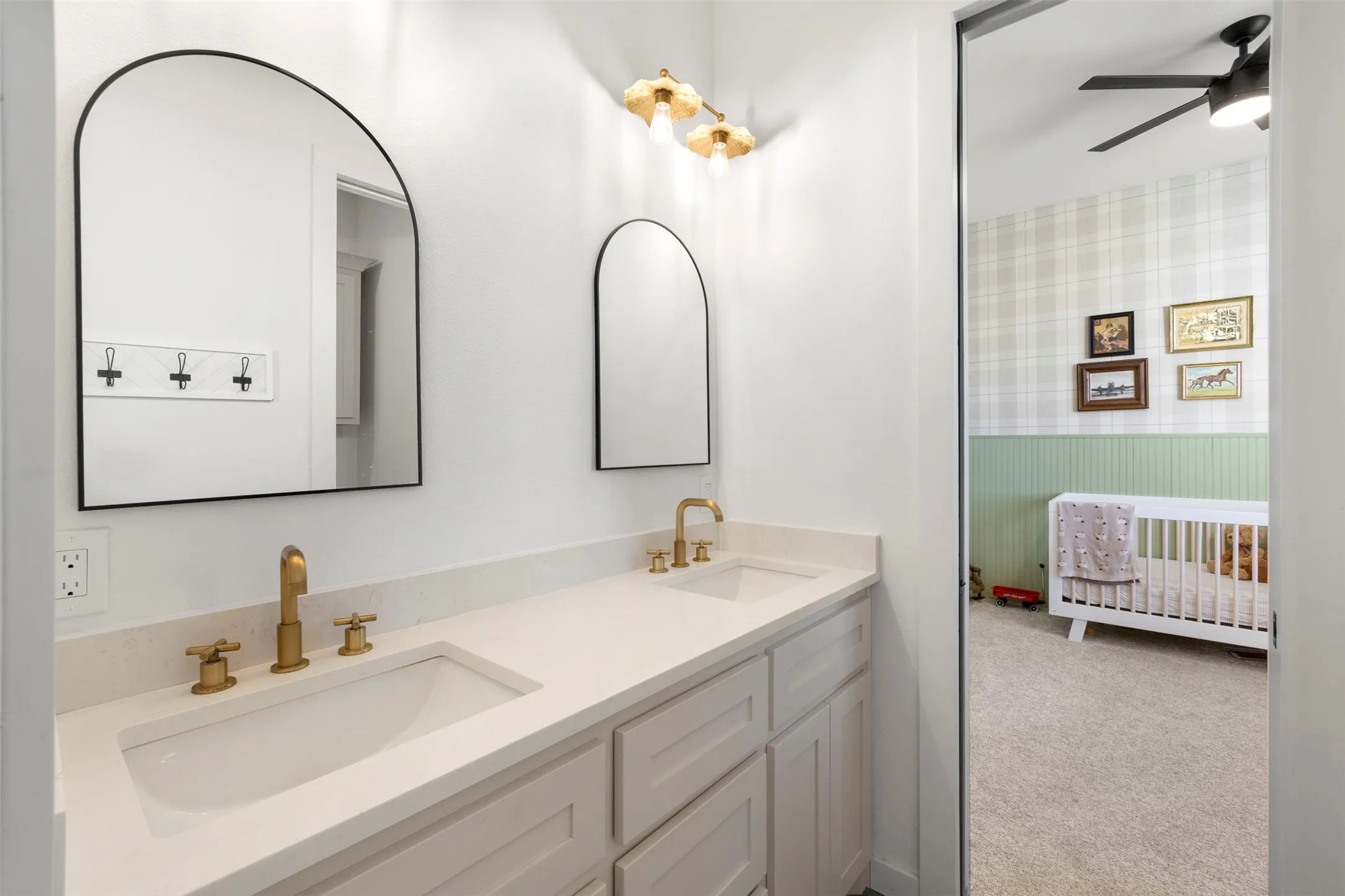 Dual vanity with integrated sinks, gold-finish fixtures, arched mirrors, and white cabinetry