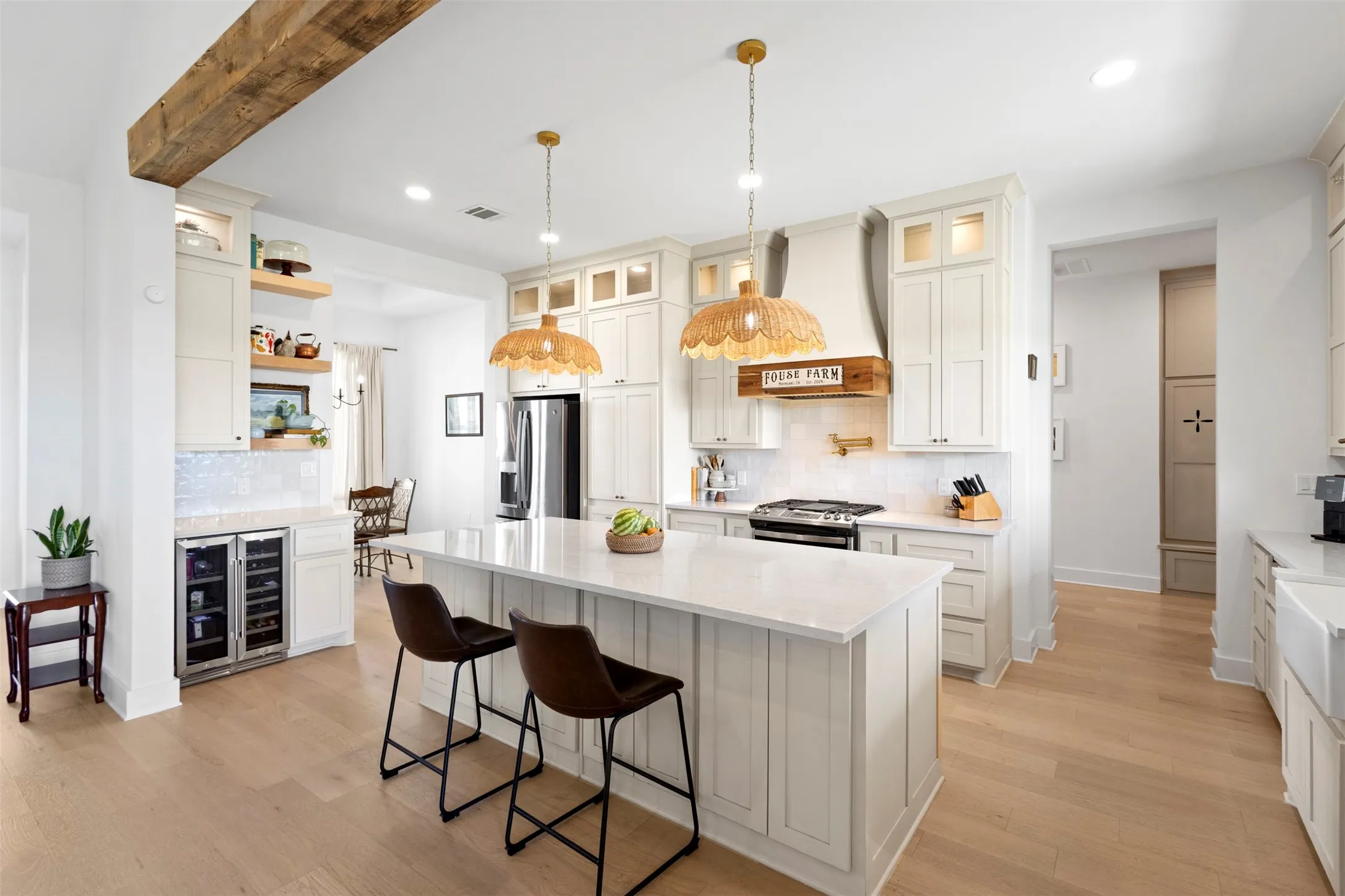 Expansive kitchen featuring an oversized island with countertop seating, light wood-finish flooring, a built-in beverage cooler, a tile backsplash, and a custom range hood