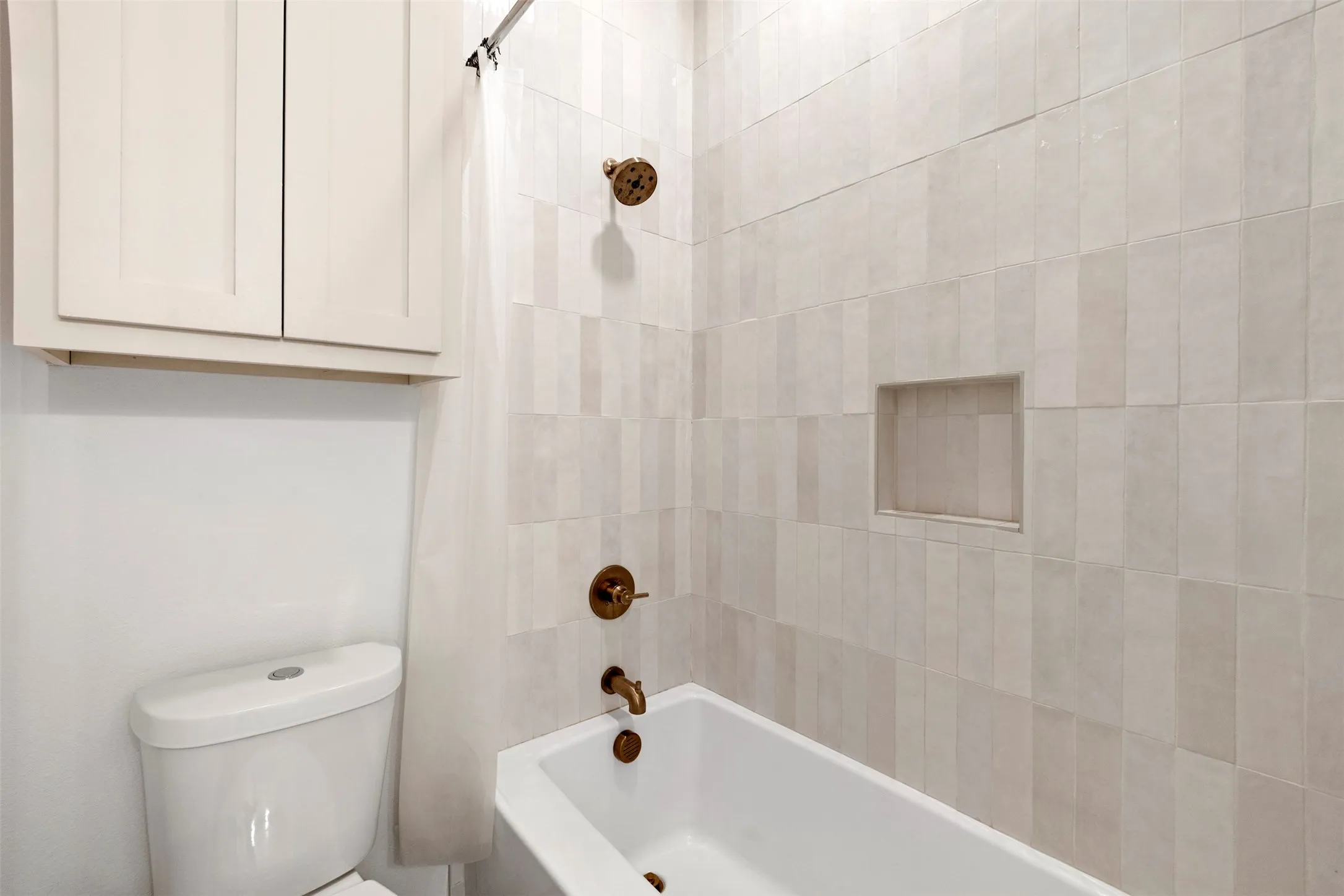 White subway tile shower surround with integrated niche, modern white bathtub, and bronze fixtures