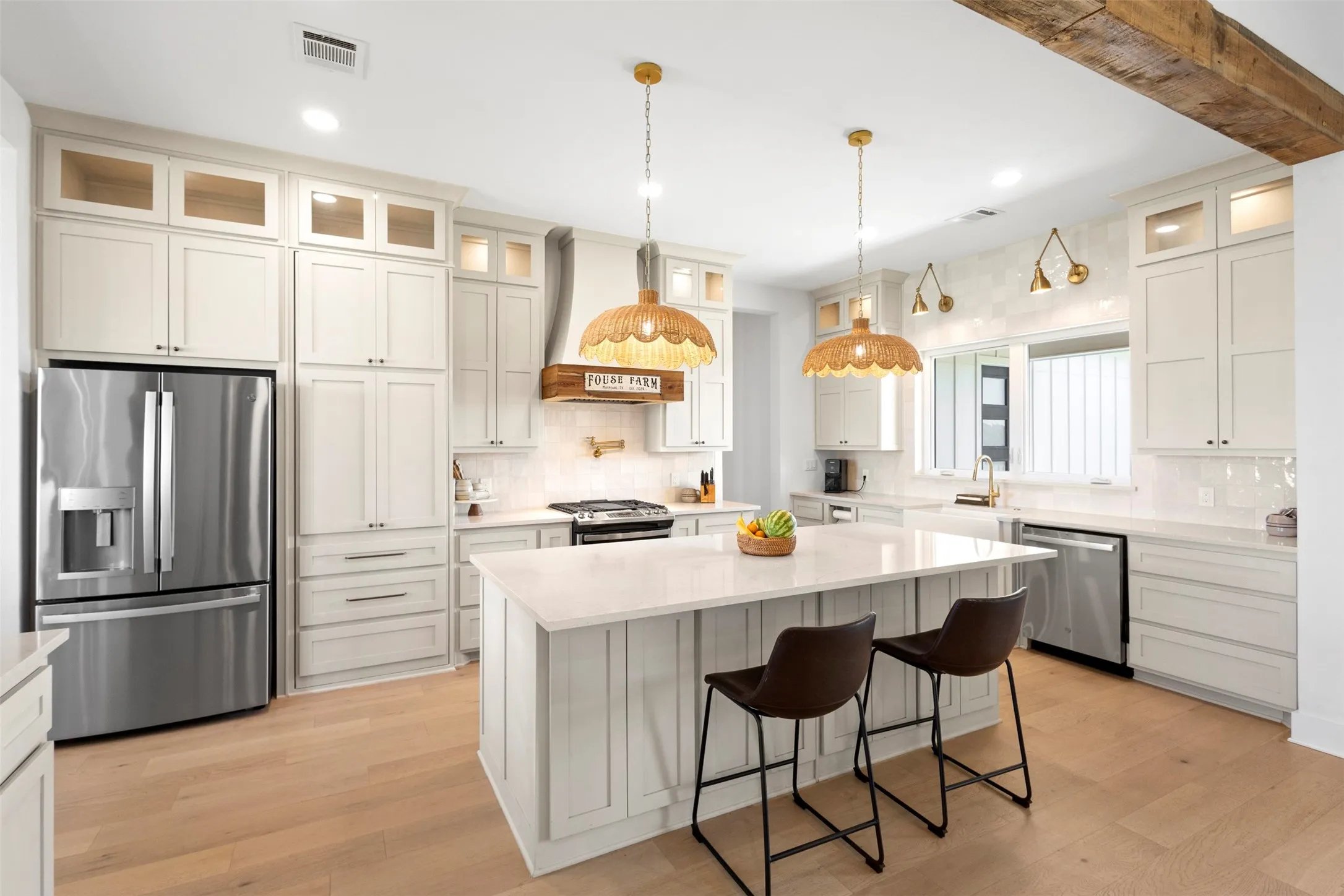 Kitchen featuring a large island with seating, stainless steel appliances, extensive cabinetry with glass-front uppers, wood-finish flooring, and a decorative exposed beam