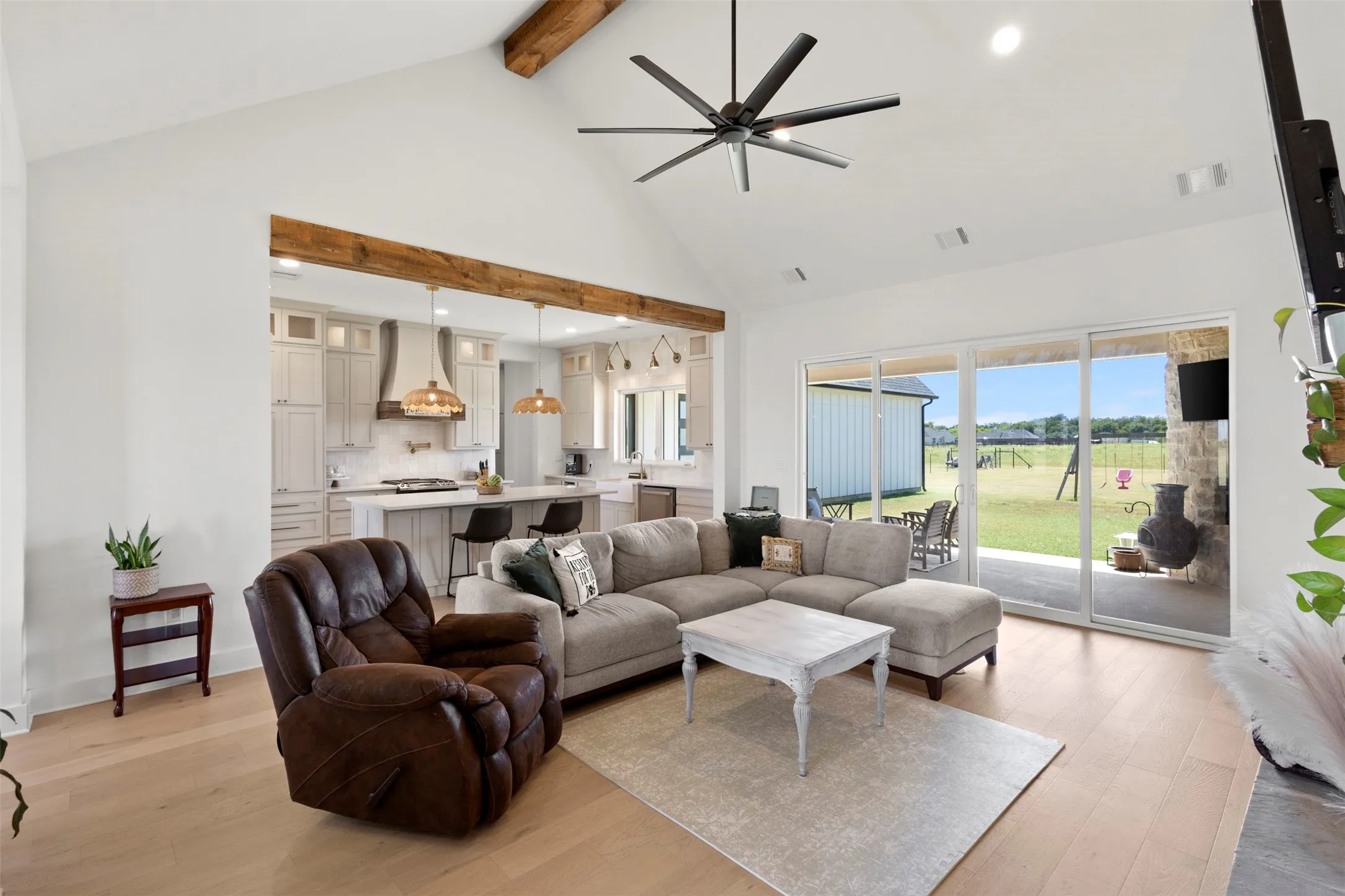 Vaulted ceiling with exposed wood beams, wood-finish flooring, recessed lighting, and expansive sliding glass doors