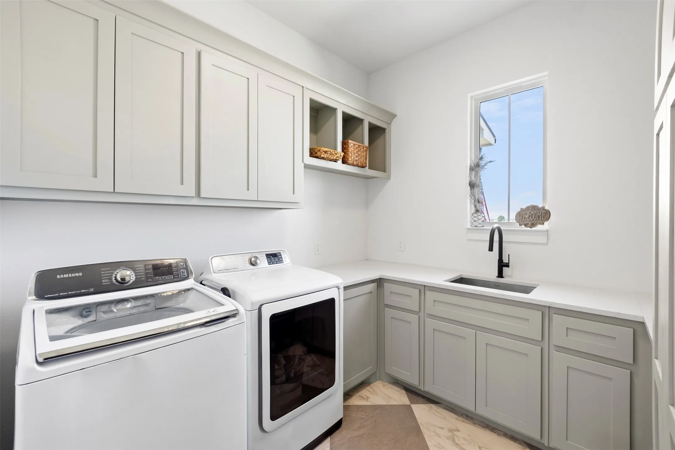 Laundry room featuring upper and lower cabinetry, a built-in sink with a matte black faucet, light-toned countertops, and checkerboard floor tiling