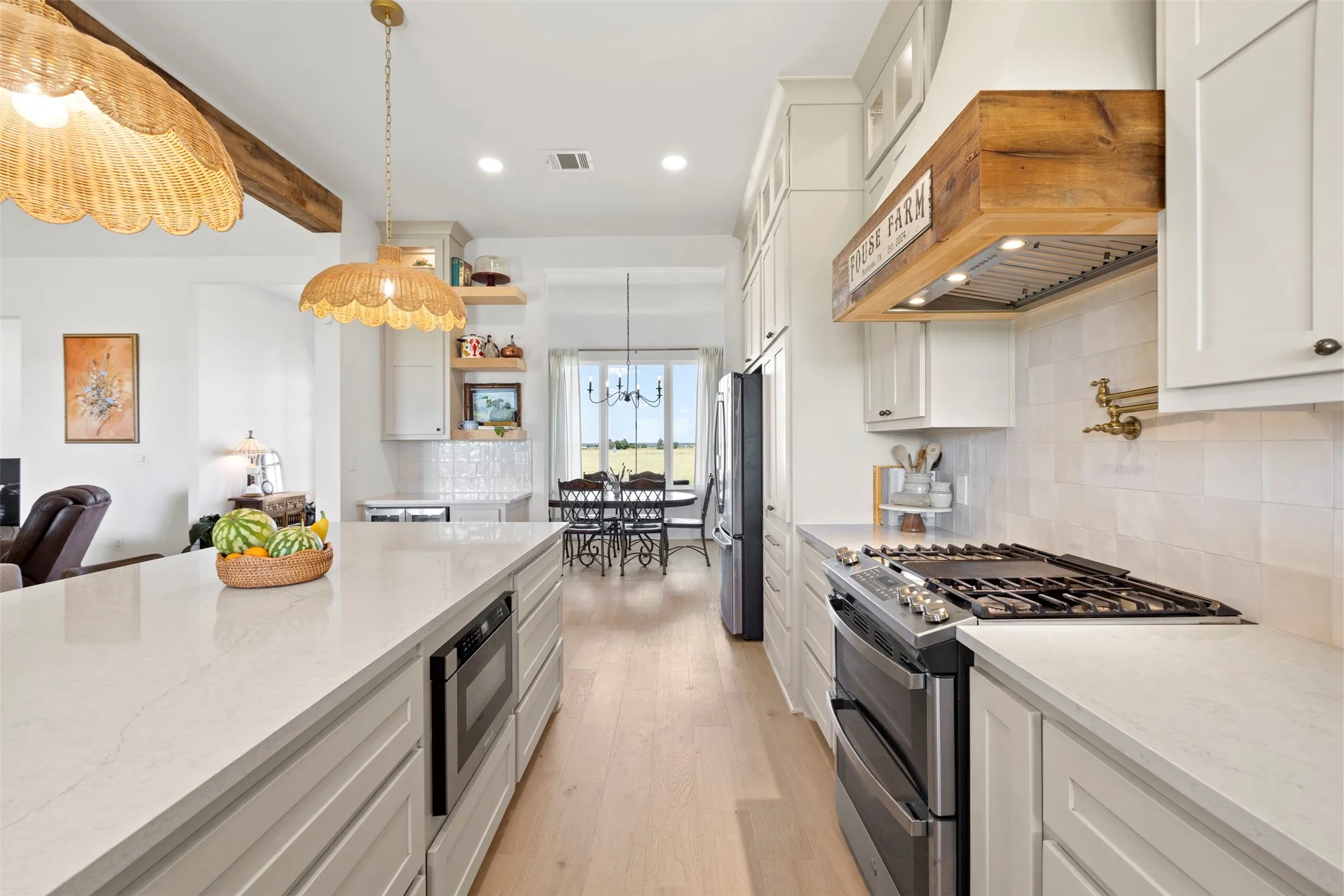 Expansive kitchen island with built-in microwave, light wood-finish flooring, white cabinetry, gas range with double ovens, and a custom wood range hood
