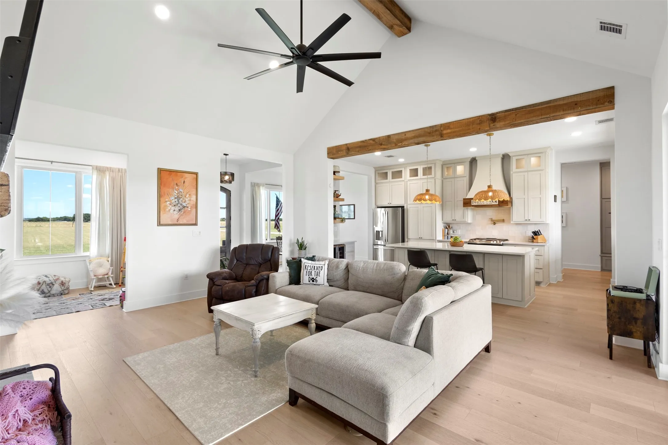 Vaulted ceiling with exposed wood beams, light wood-finish flooring, recessed lighting, kitchen with built-in cabinetry and island seating, and a modern ceiling fan