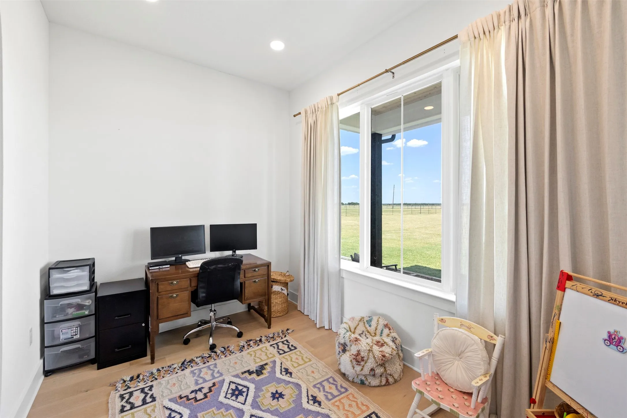 Recessed lighting illuminates a versatile room featuring light wood-finish flooring and a large window