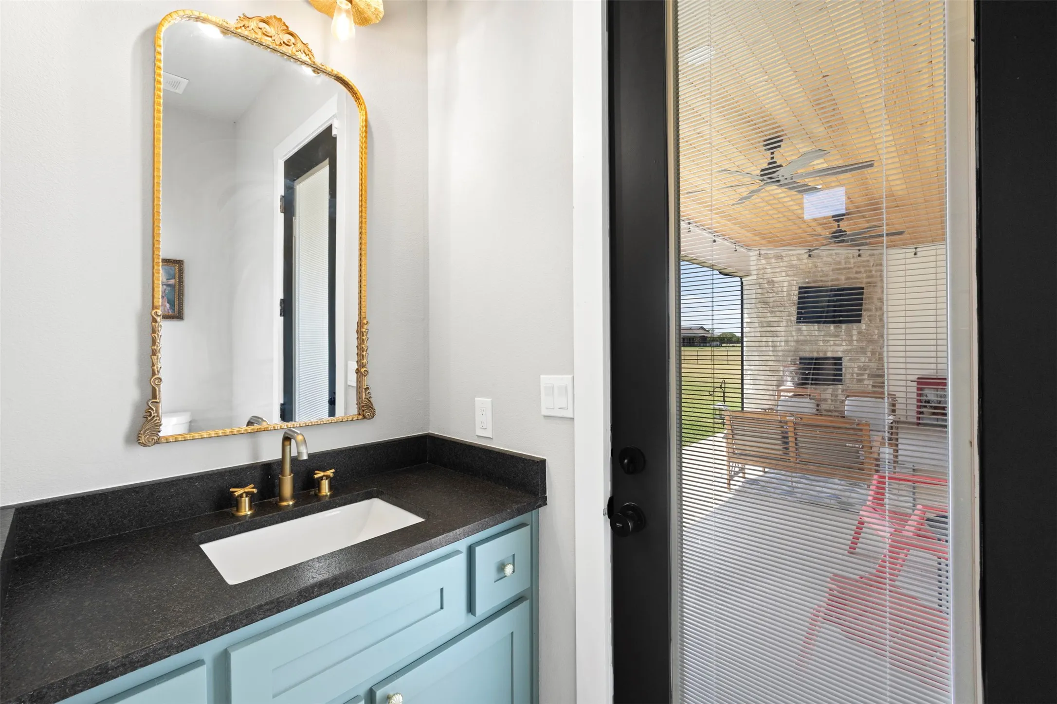 Powder room featuring a gold-framed mirror, brass-finish faucet, and a light blue vanity with a dark countertop