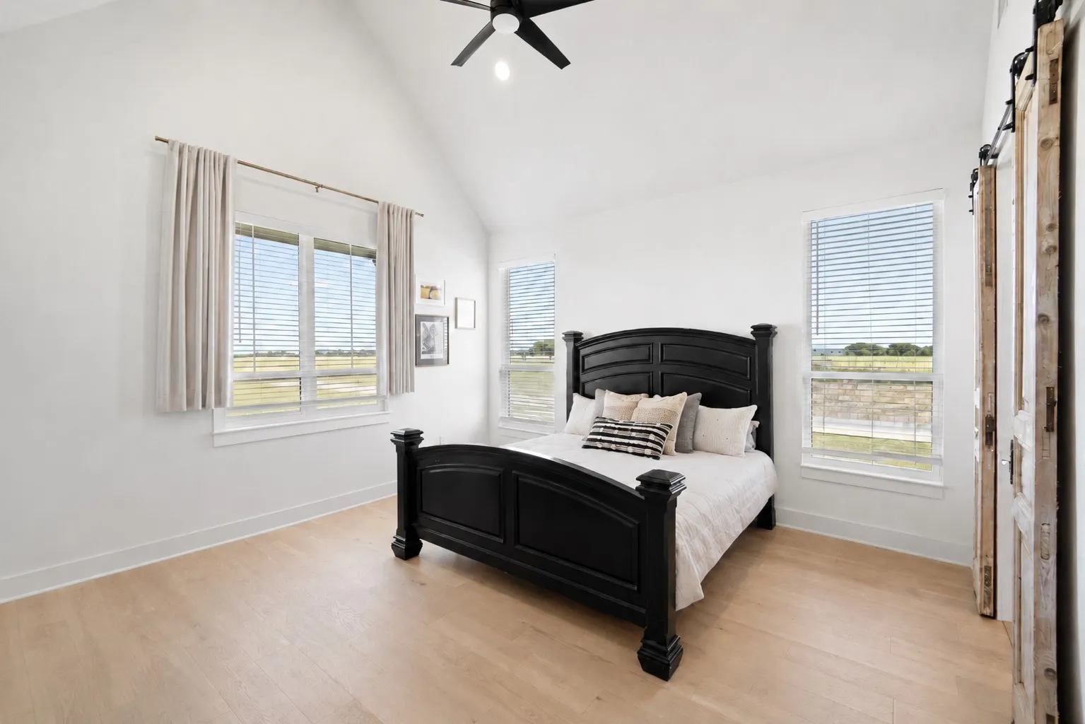 Vaulted ceiling with a ceiling fan, multiple windows with blinds, wood-finish flooring, and a barn door