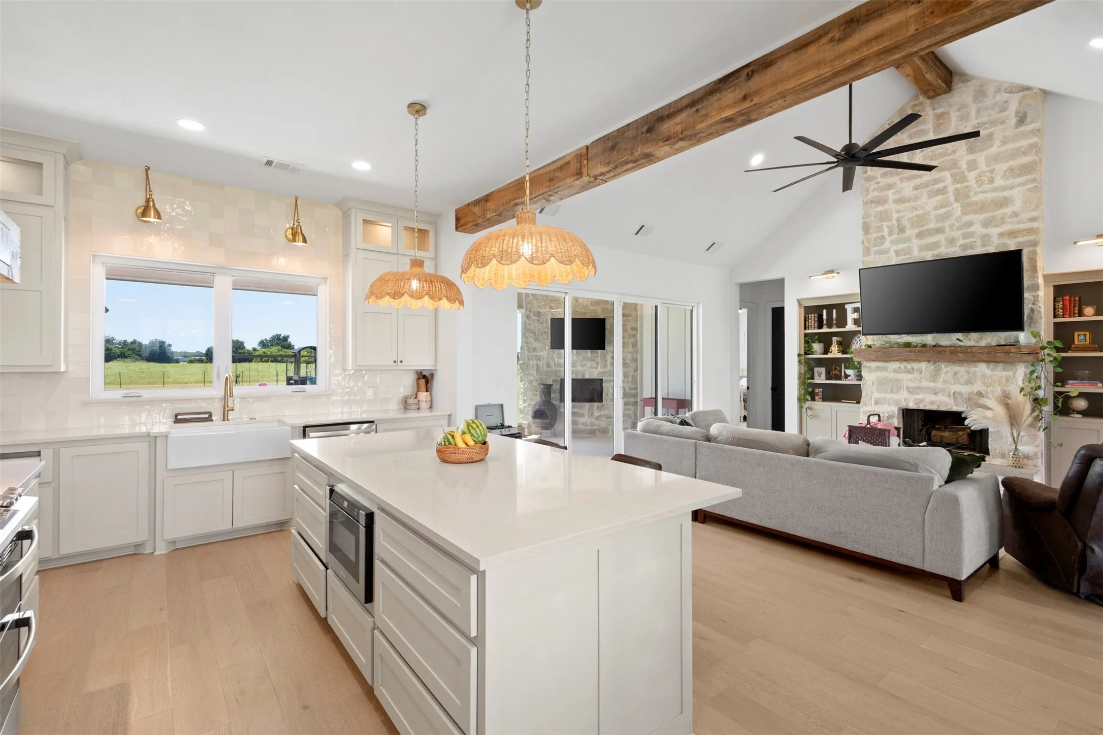 Open-concept living area featuring a stone fireplace, vaulted ceiling with exposed wood beams, and wood-finish flooring