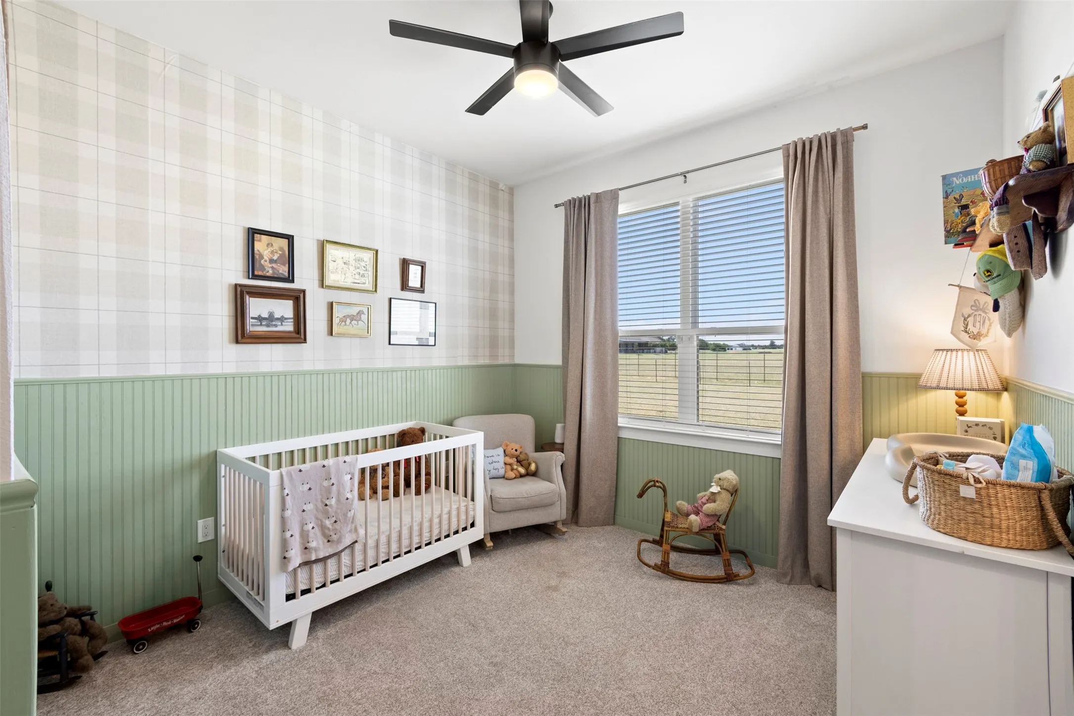 Carpeted room with a ceiling fan, window with blinds, and two-tone wall treatment featuring wainscoting and plaid wallpaper