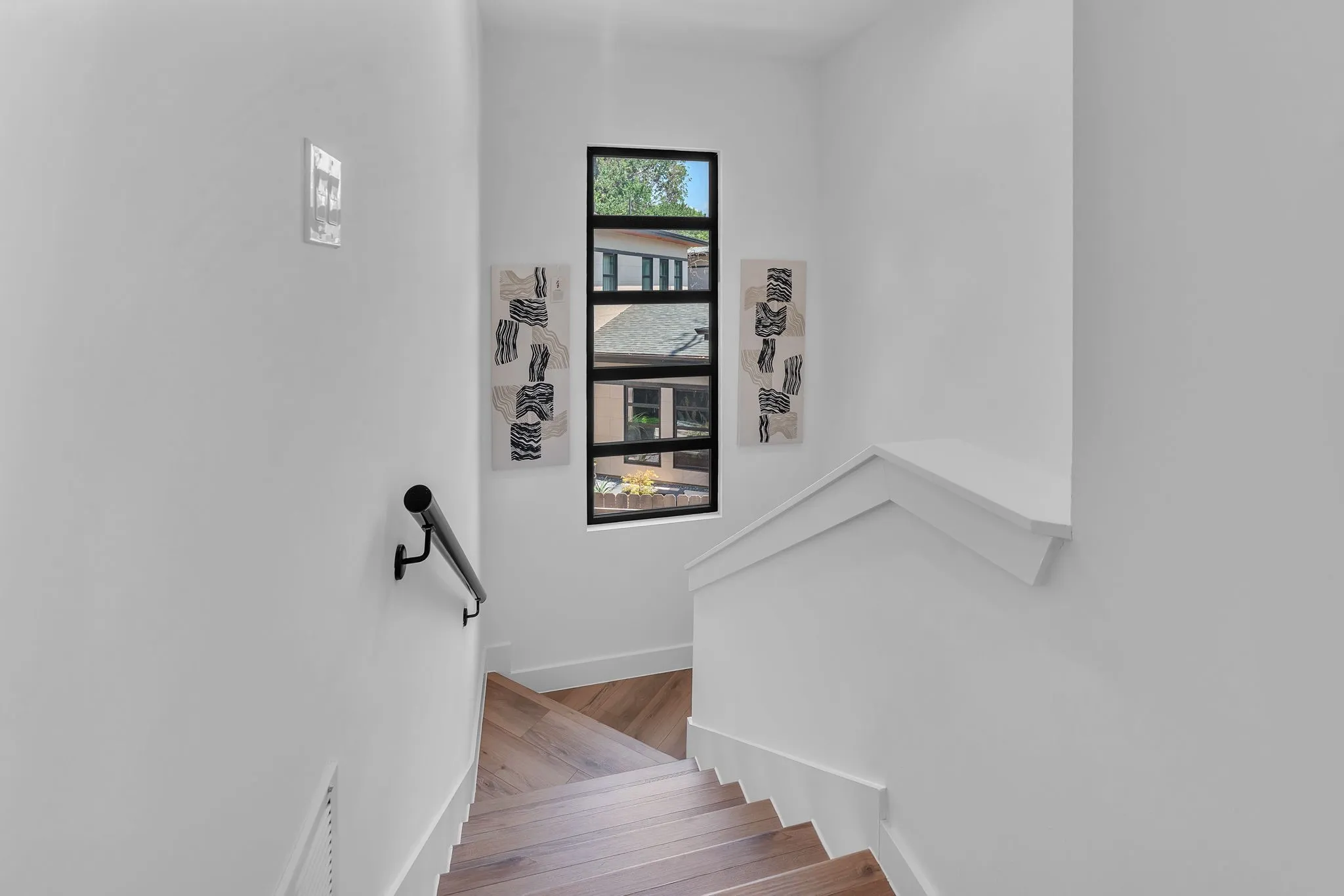 Staircase featuring wood-finish treads, a black handrail, and a tall multi-pane window
