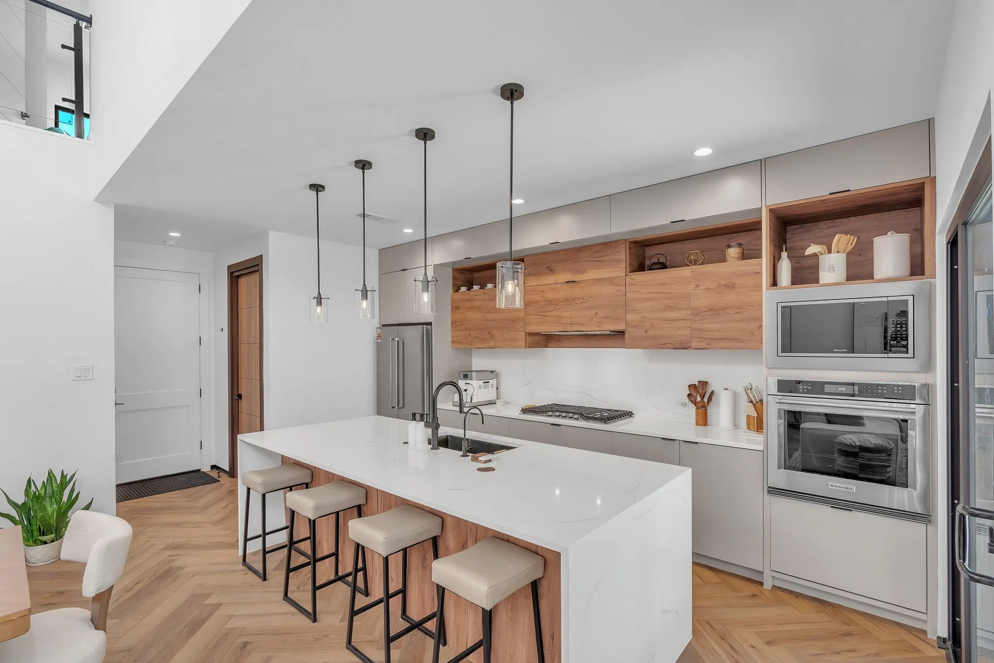 Contemporary kitchen featuring wood-finish flooring, a waterfall island with a white countertop, and pendant lighting