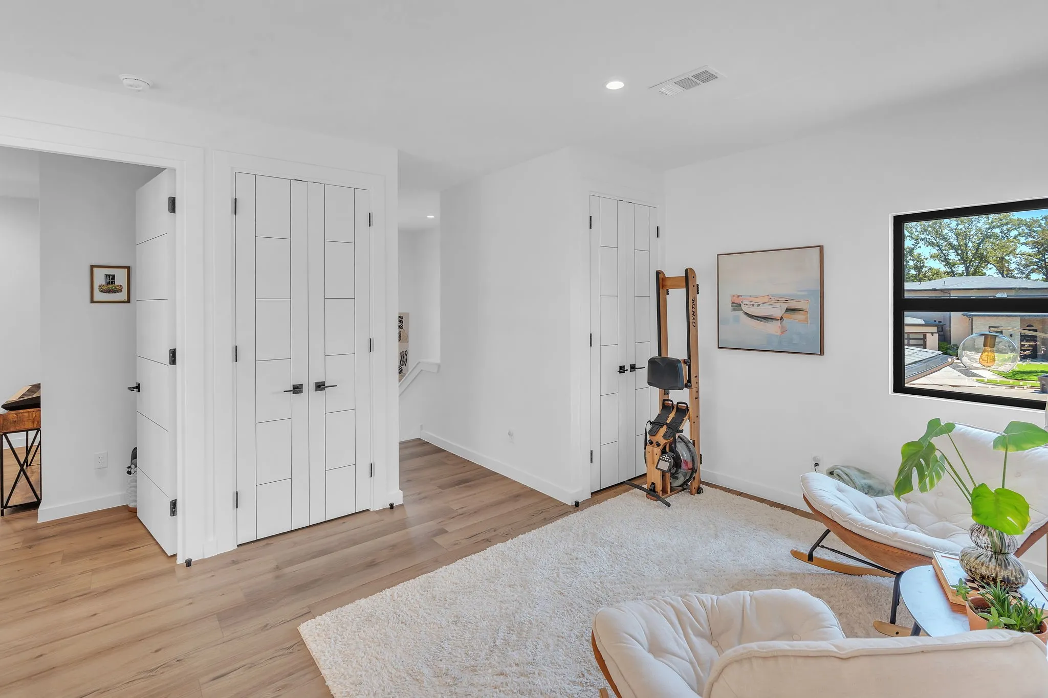 White interior walls, wood-finish flooring, recessed lighting, and a black-framed window