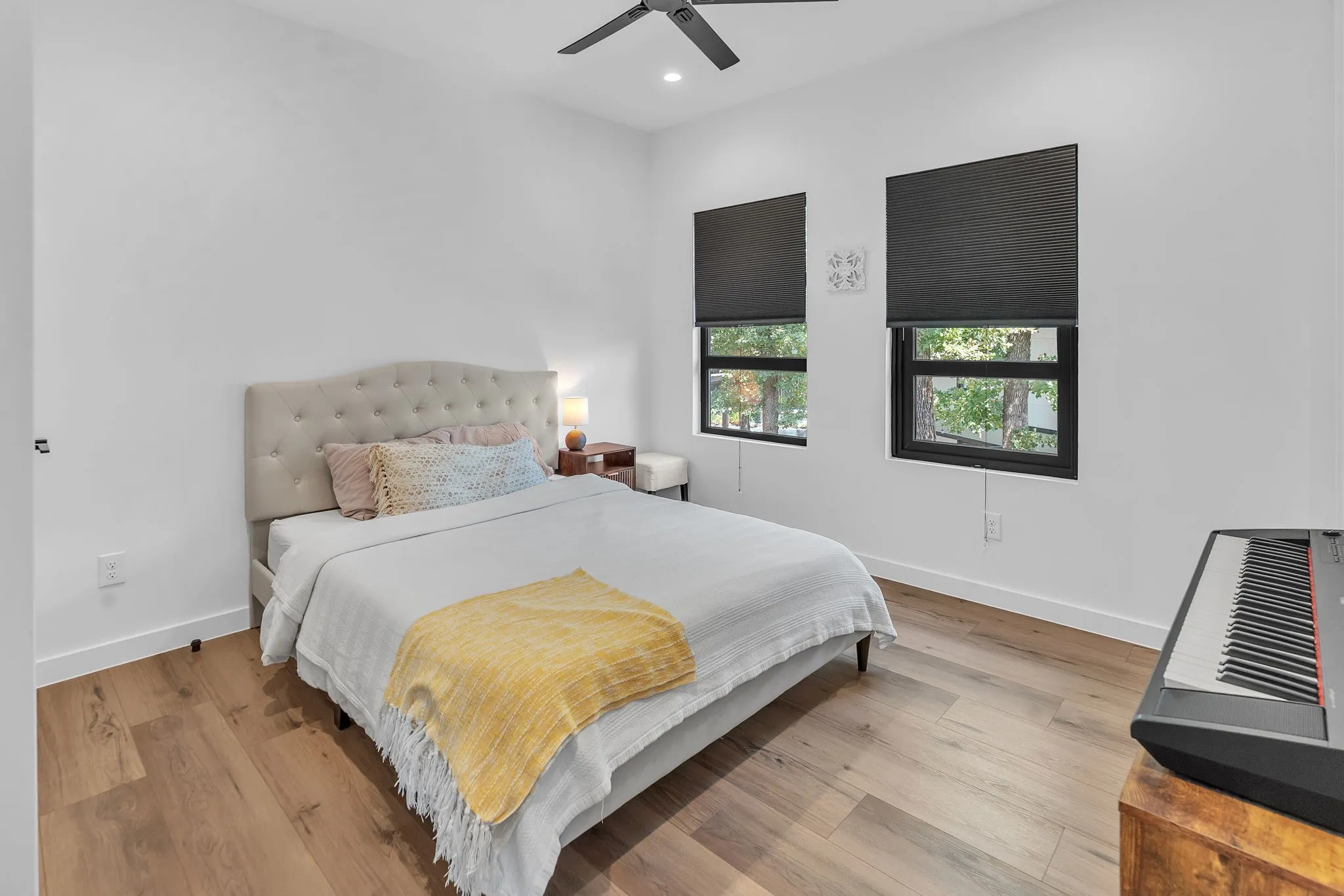 Ensuite Bathroom, Wood-finish flooring, two large windows with dark blinds, a ceiling fan, and a light-colored upholstered headboard