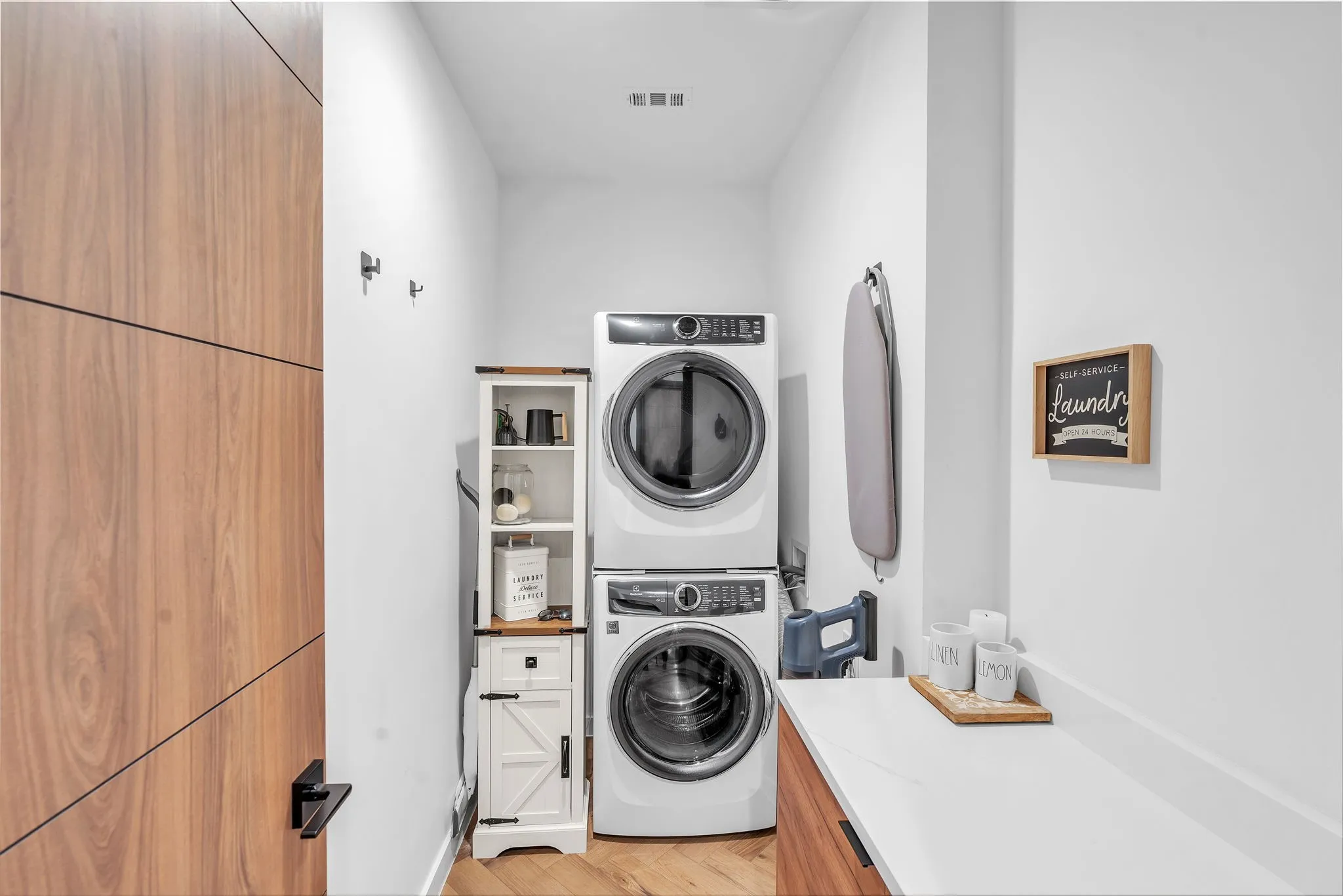 Laundry area featuring wood-finish flooring, stackable appliances, white countertop, and built-in wood-finish cabinetry