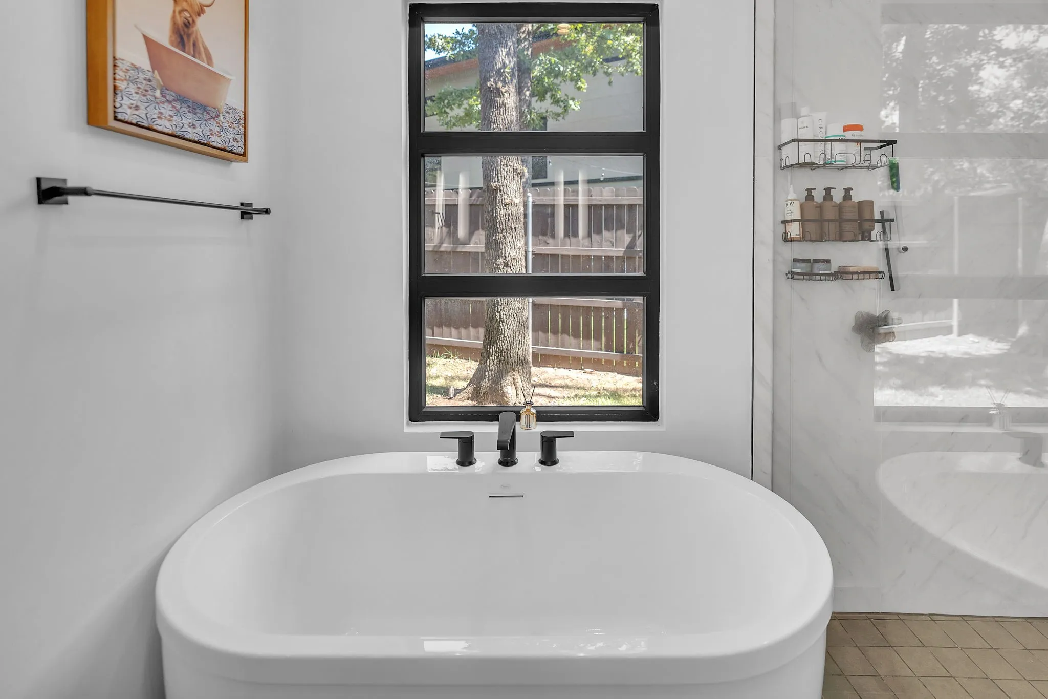 Freestanding oval soaking tub with matte black fixtures, adjacent to a contemporary black-framed window