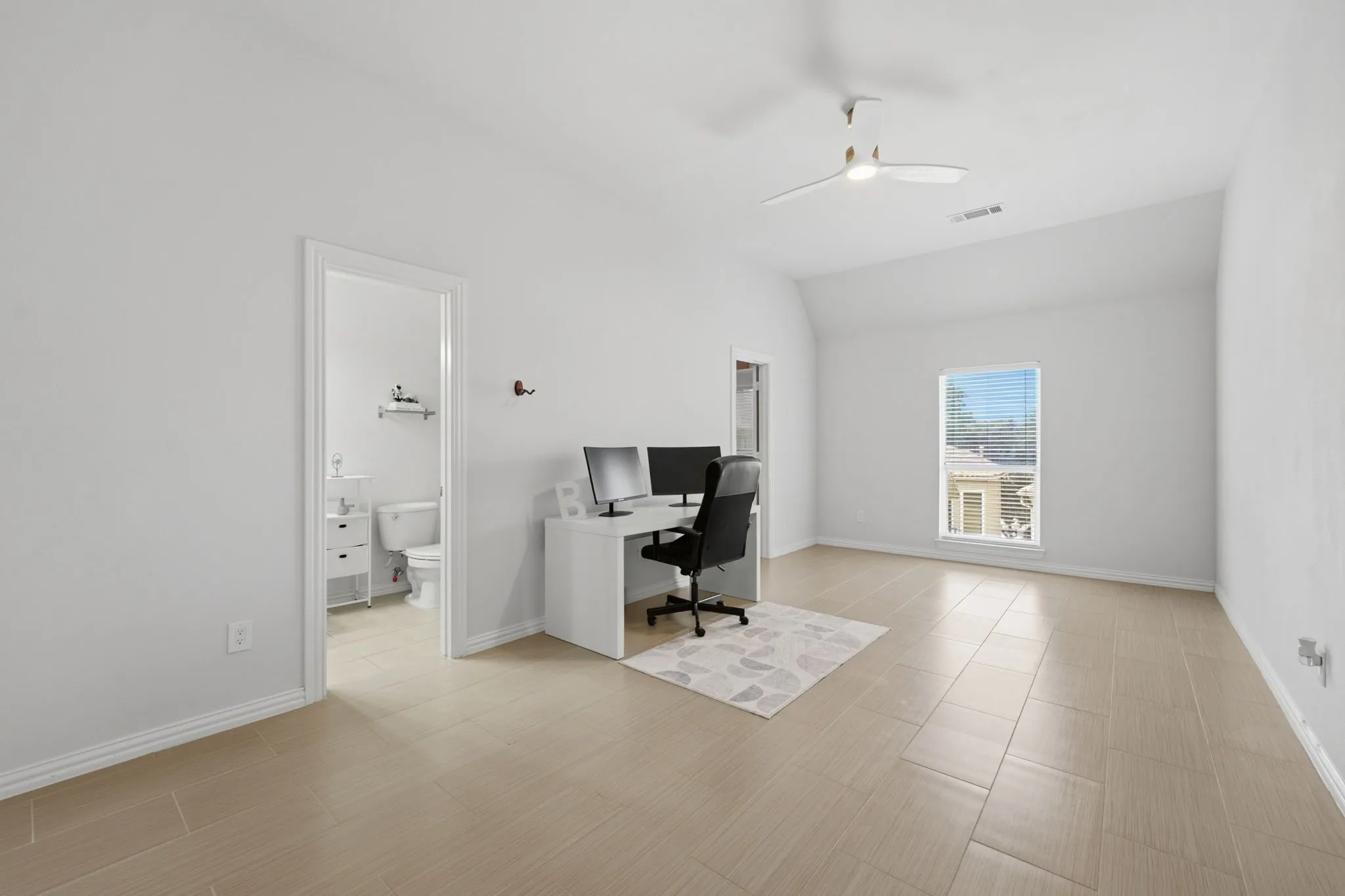 Spacious room featuring light-toned tile flooring, a sloped ceiling, and a ceiling fan