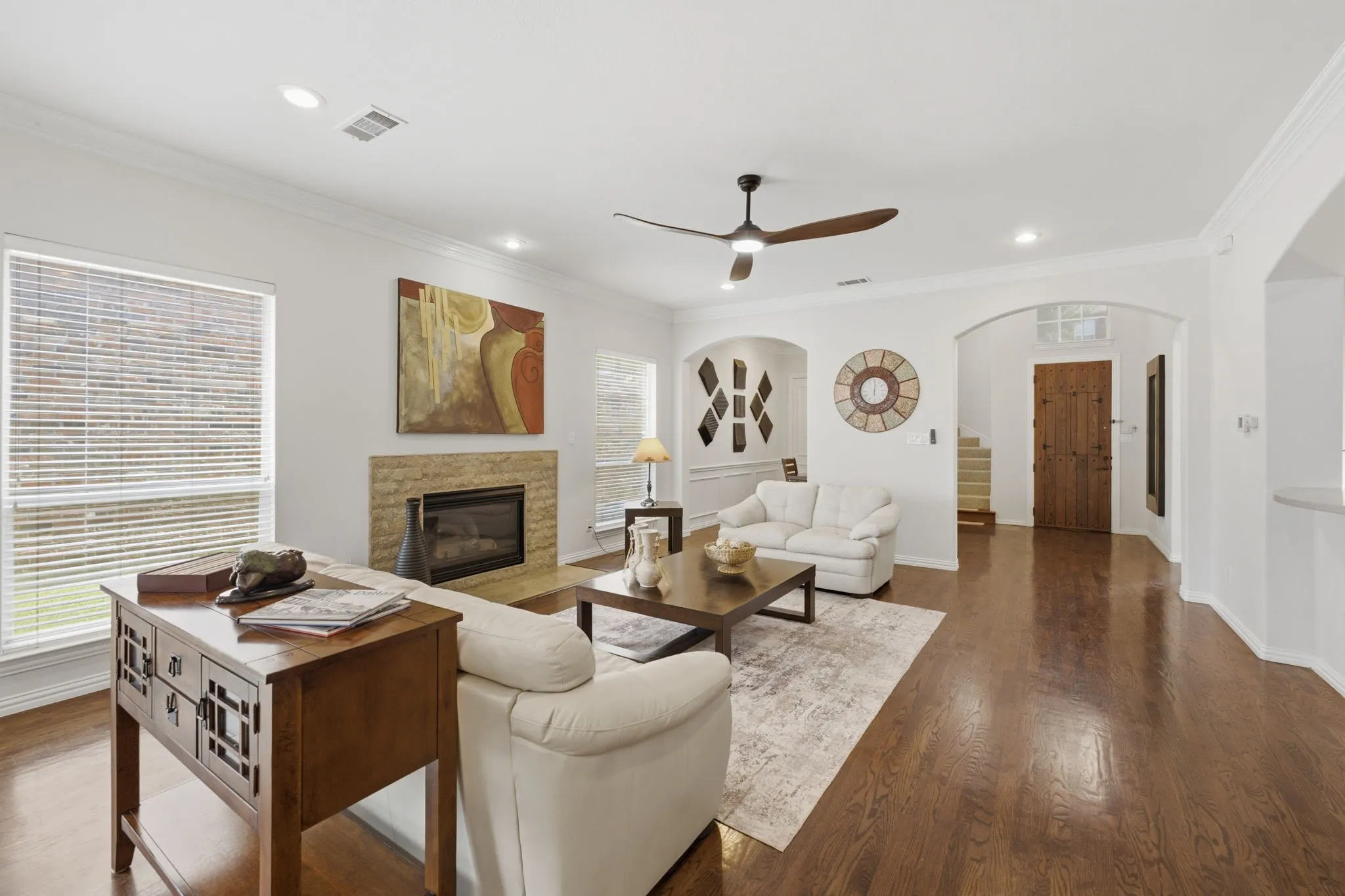 Spacious living area featuring wood-finish flooring, a fireplace with stone surround, recessed lighting, and a ceiling fan
