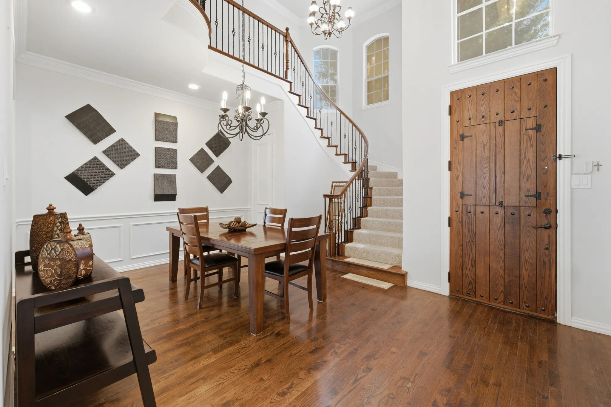 Hardwood flooring, wainscoting, wrought iron baluster staircase, wood panel door, and high ceilings