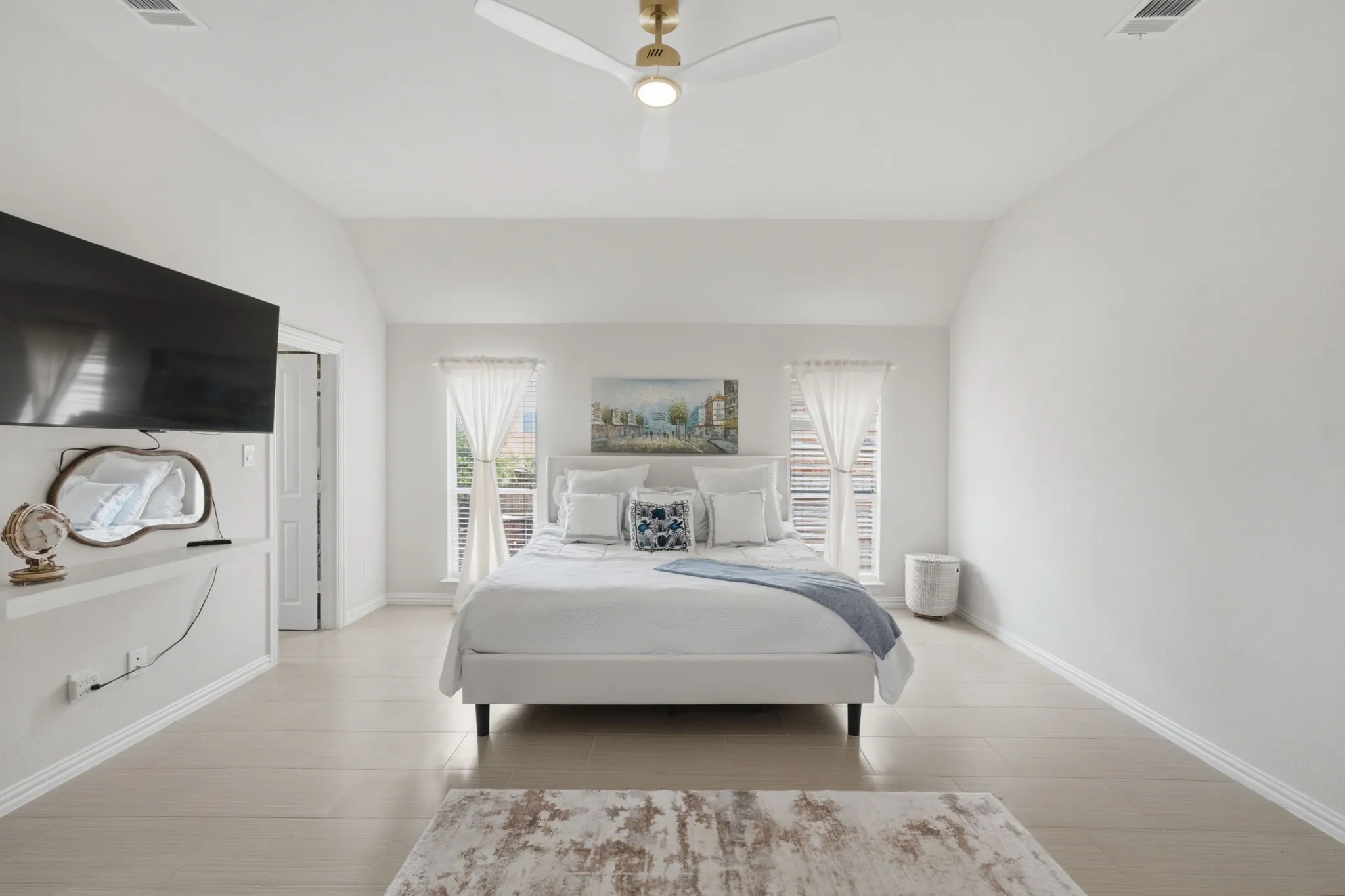 Vaulted ceiling with a gold-tone ceiling fan, light-toned wood-finish flooring, and two windows with sheer privacy curtains