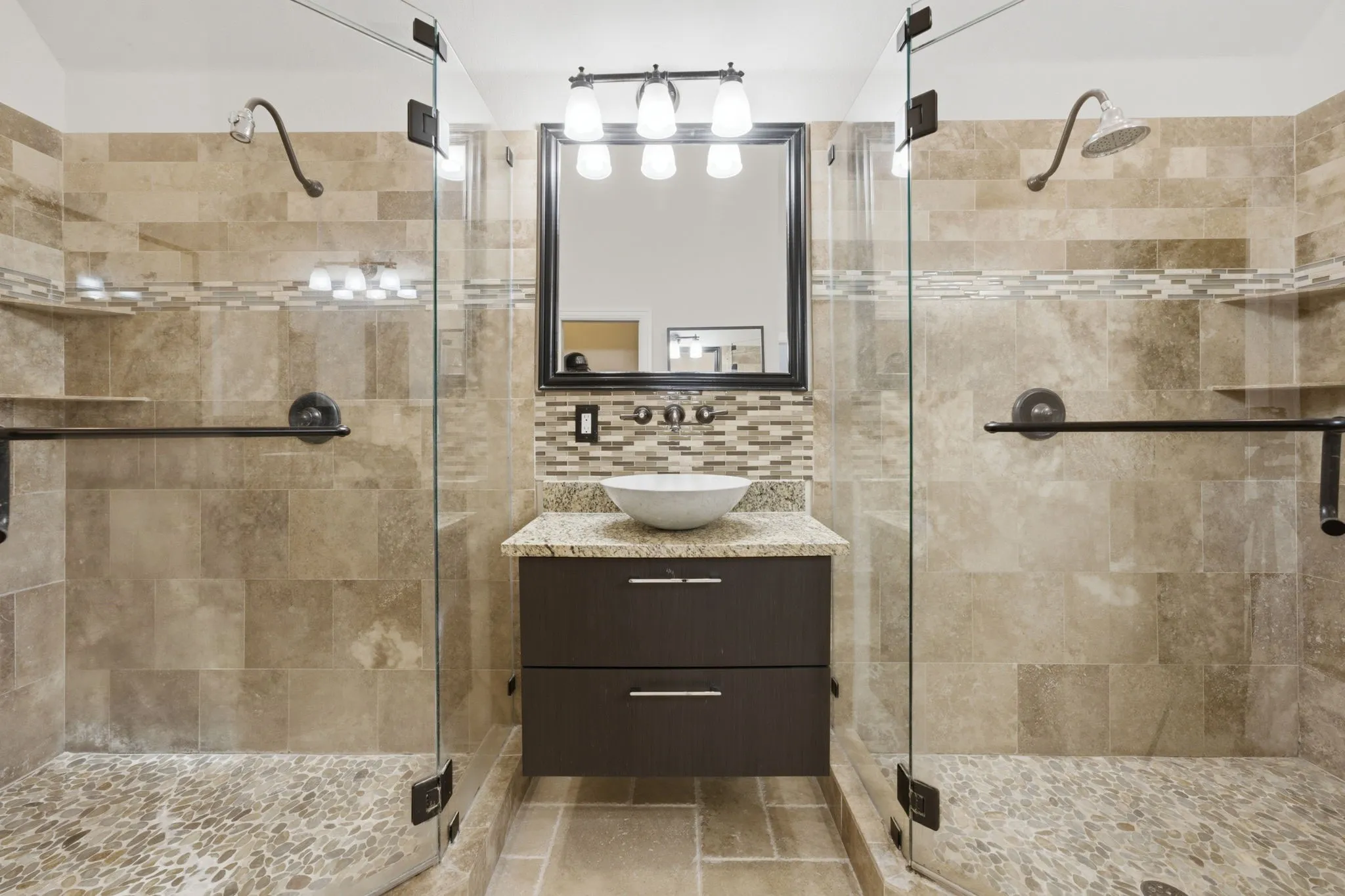 Dual glass-enclosed showers with pebbled flooring and integrated shelving